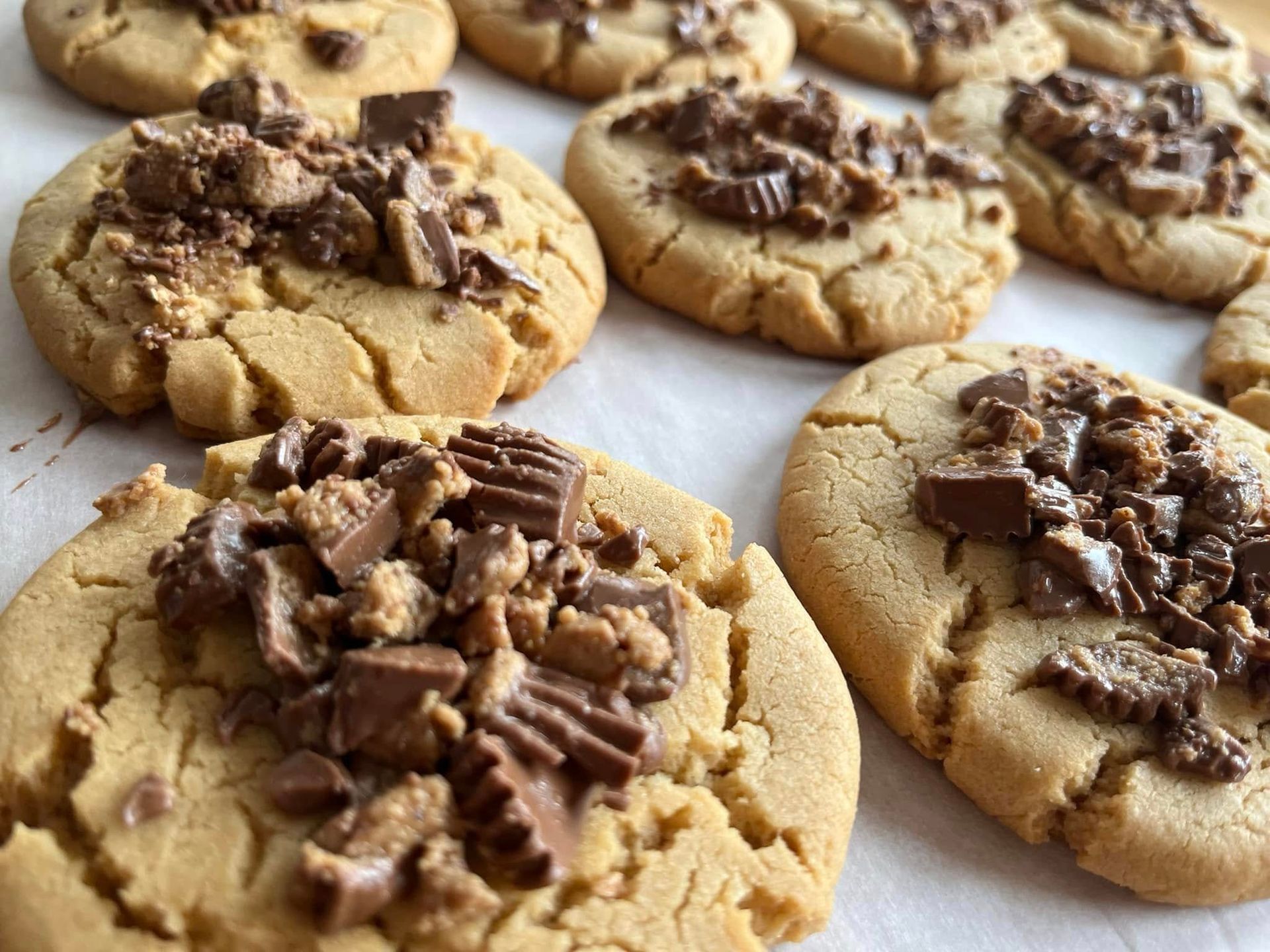 Peanut butter cookies topped with chopped peanut butter cups on parchment paper.
