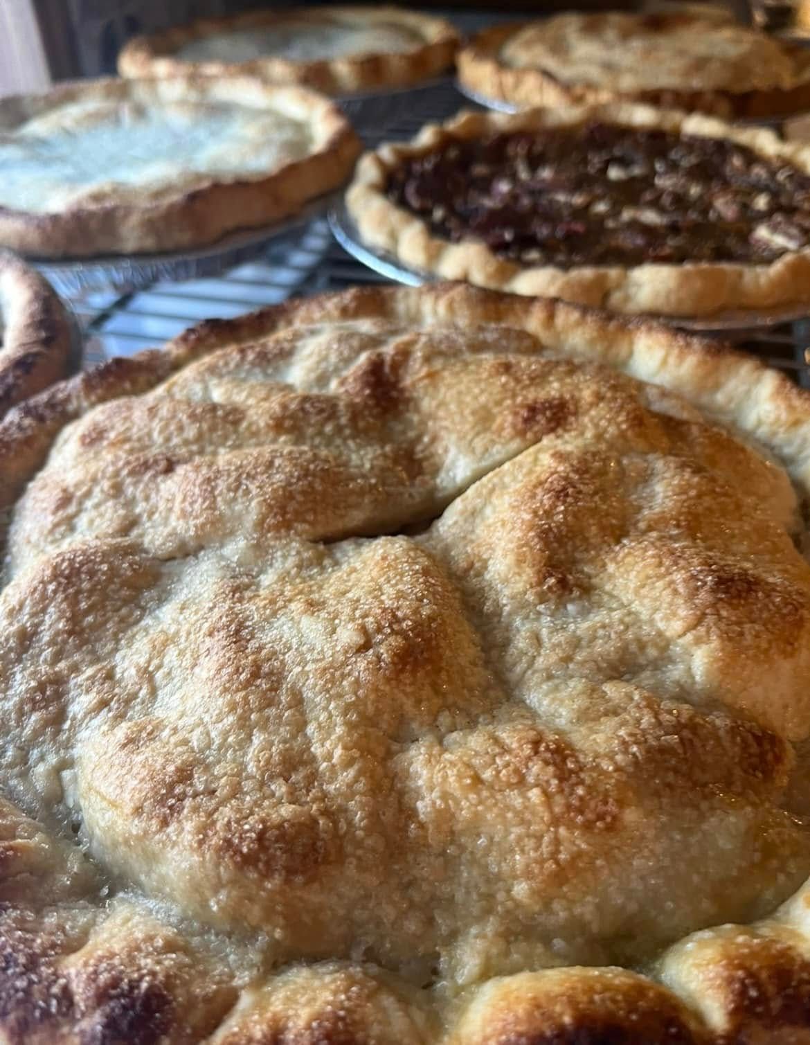 Close-up of a golden-brown pie with several other pies in the background, all on a metal rack.