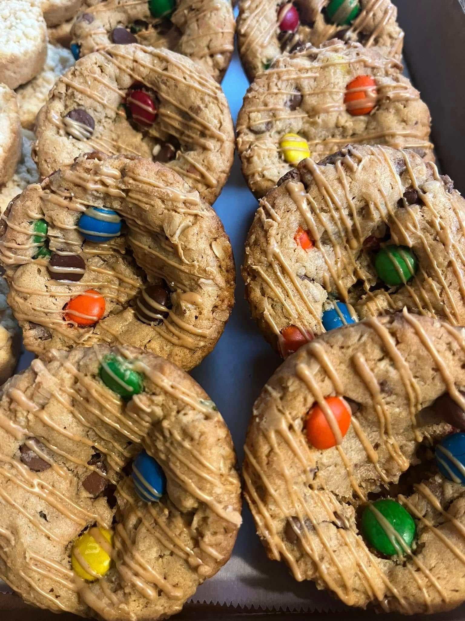 Close-up of a tray of round, decorated cookies with chocolate chips and candies, drizzled with caramel.