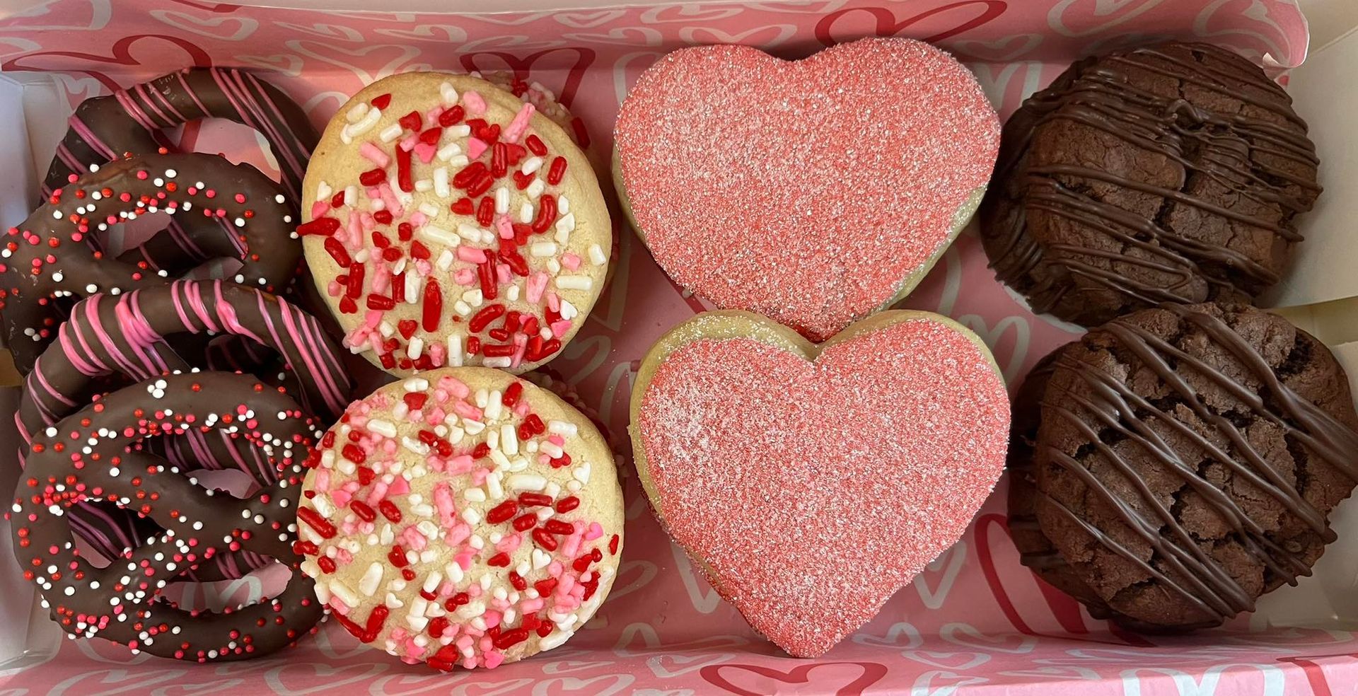 Valentine's Day cookie box: chocolate-covered pretzels, frosted circles with sprinkles, and pink heart cookies.