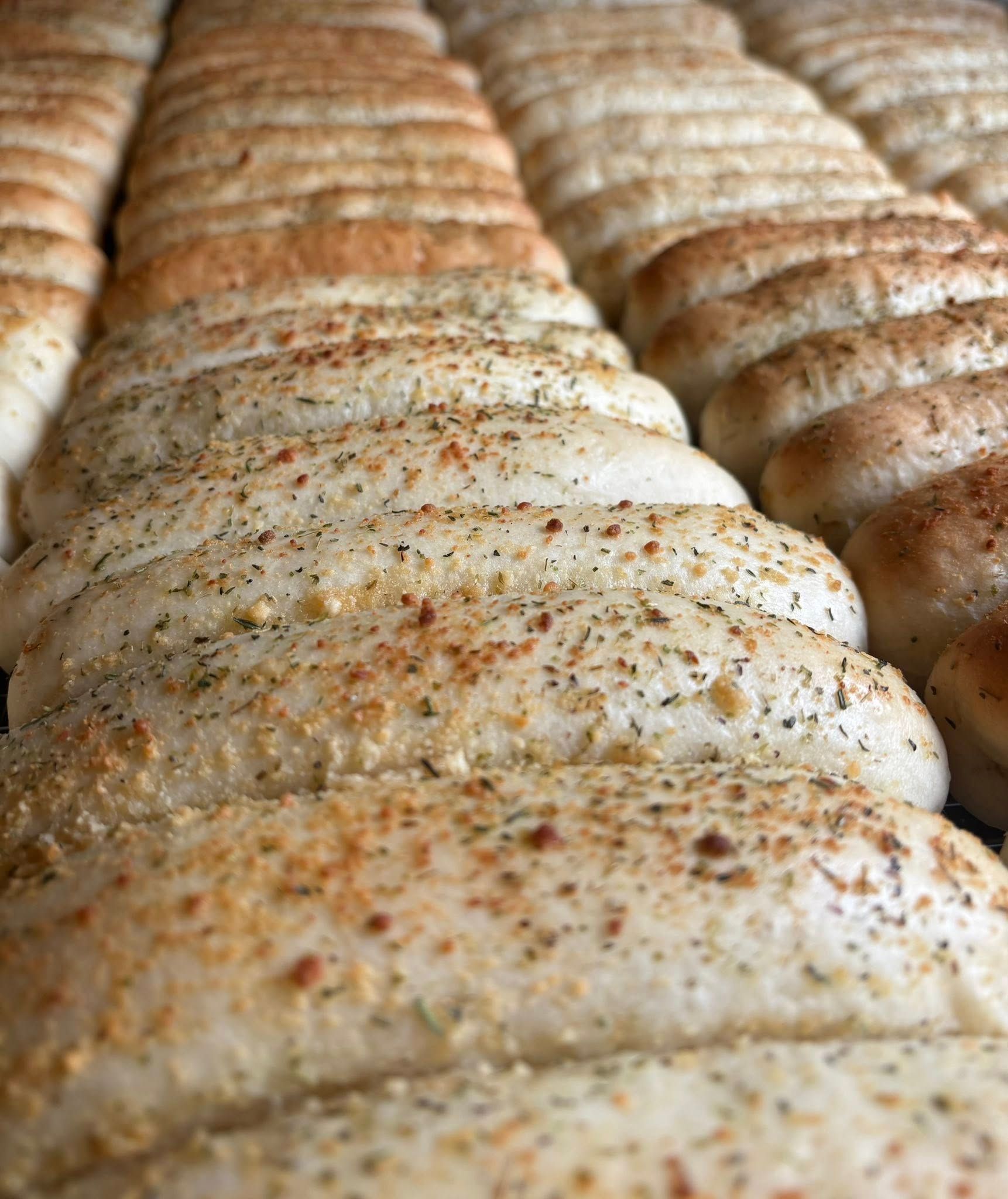 Rows of freshly baked breadsticks, seasoned with herbs and spices.