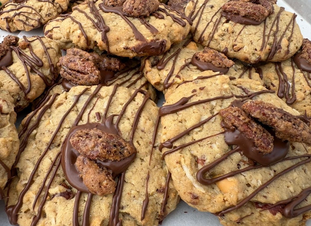 Close-up of a pile of cookies. Light brown, with chocolate drizzle and pecan halves.