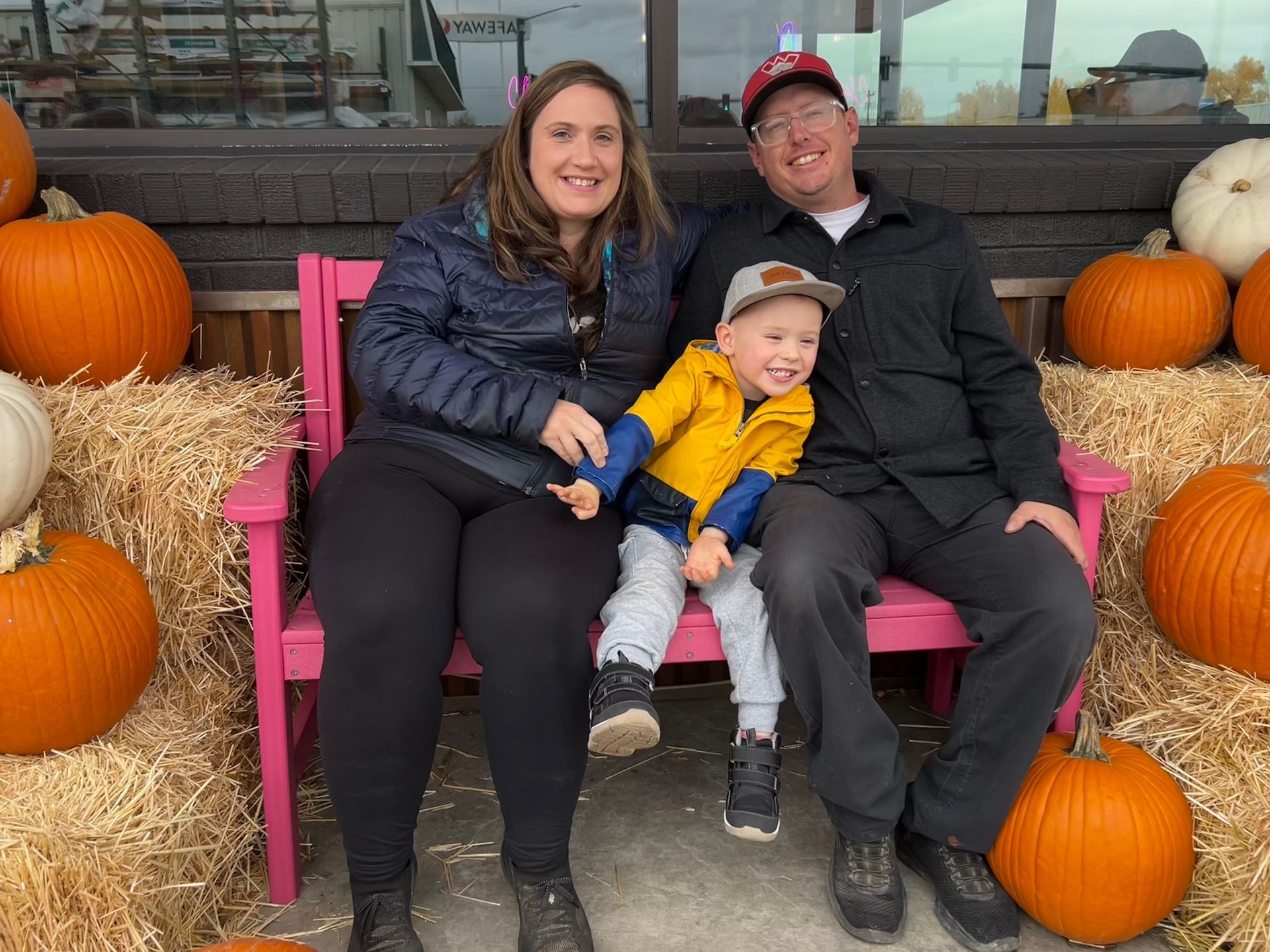 Family of three smiling, posing on a pink bench with pumpkins and hay bales. Base Camp Bakery Gunnison, Colorado https://share.google/AgqUzUKNzsb0ThlP5, https://www.facebook.com/BaseCampBakery1, https://www.instagram.com/basecampbakery_81230
