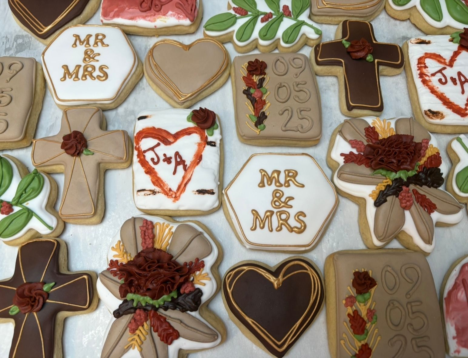 Wedding cookies decorated with white, brown, and gold frosting, with hearts, crosses, and 