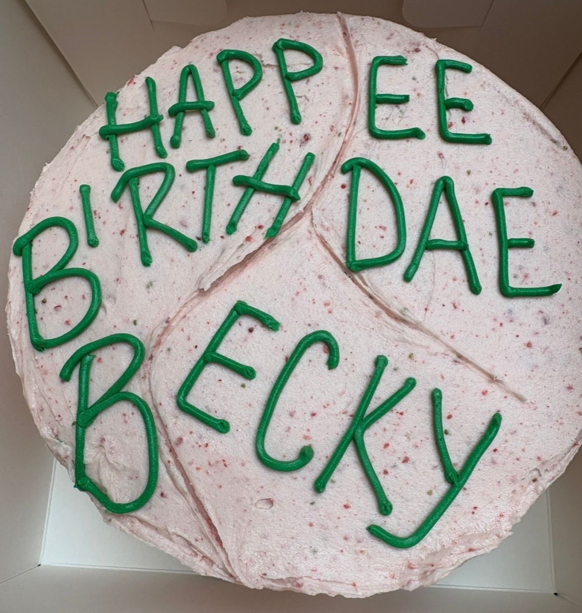 Pink frosted cake with green icing that says 