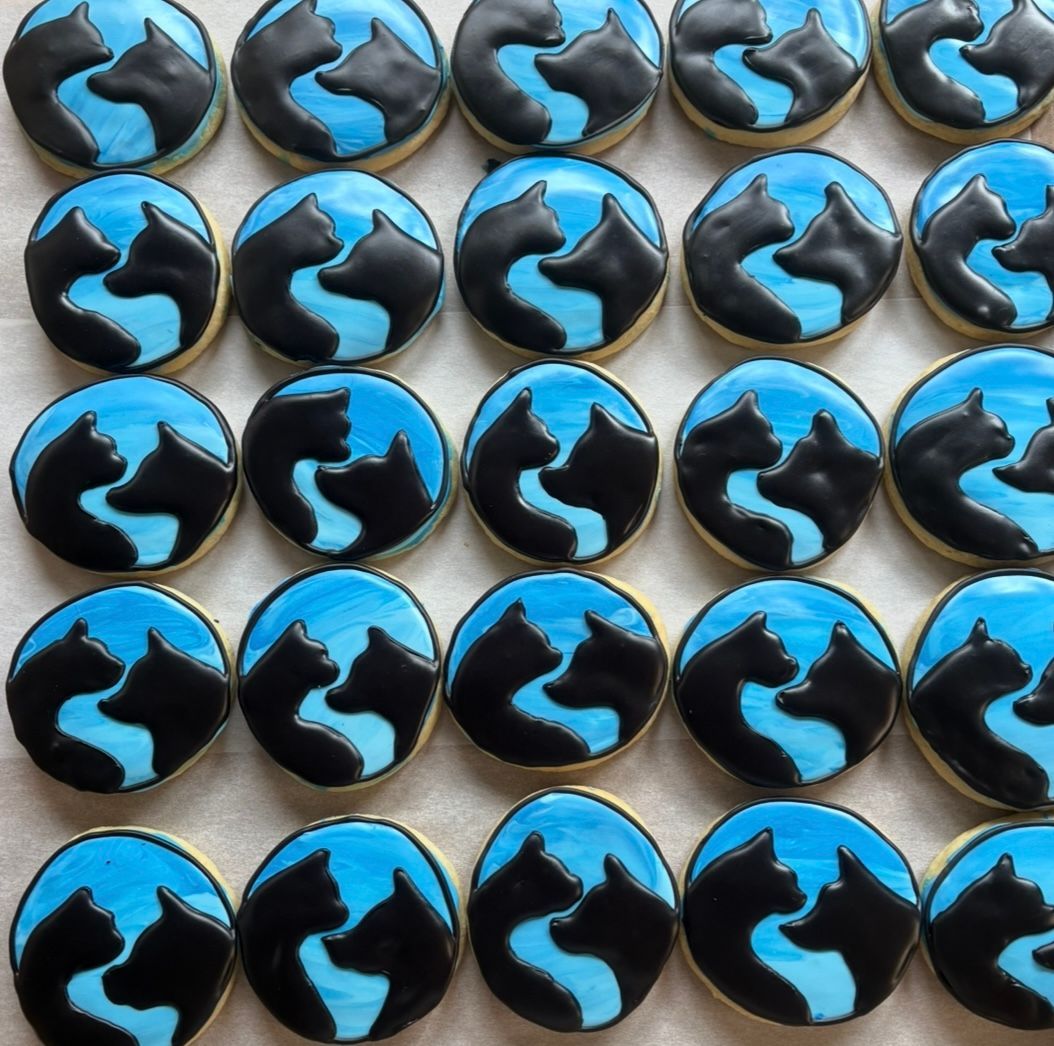 Round cookies decorated with black cat silhouettes on blue backgrounds.