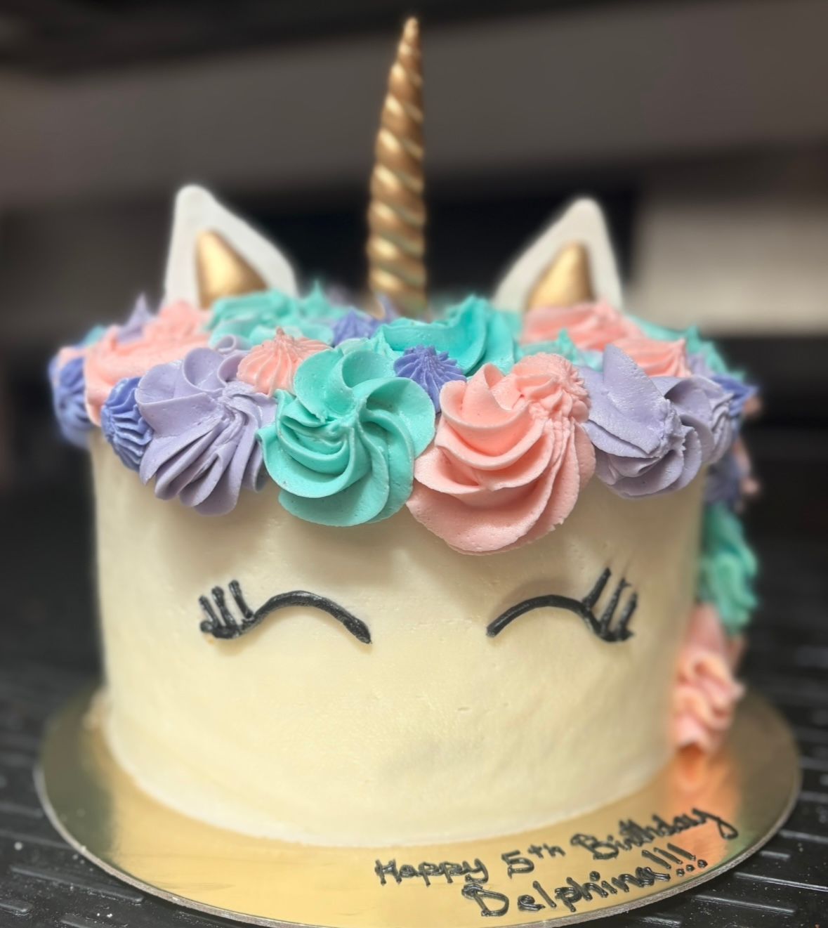 Unicorn cake with frosting mane of pink, teal, and purple rosettes. Gold horn and ears. 