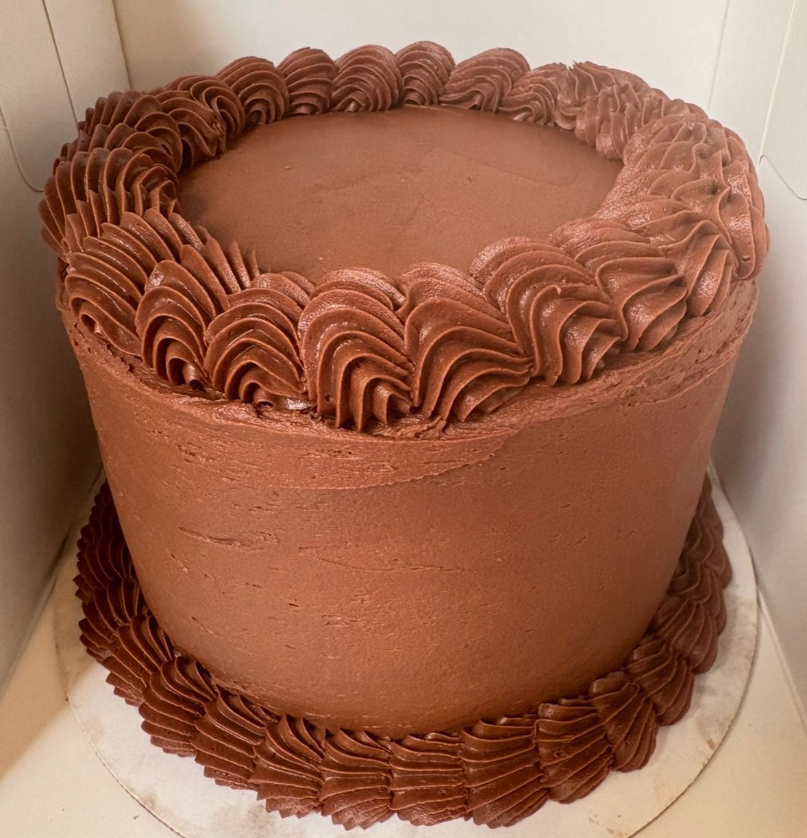 Chocolate cake with smooth frosting and decorative piped border.