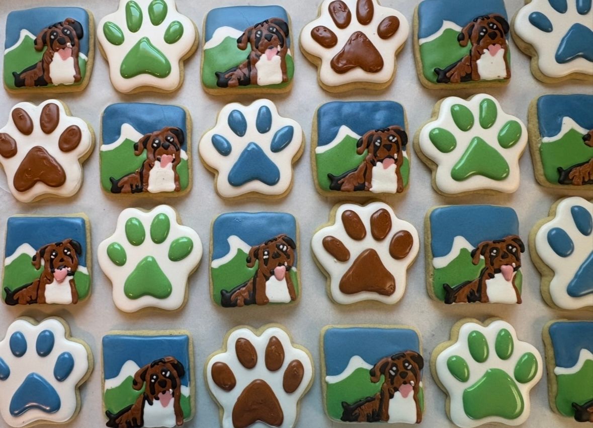 Cookies decorated with paw prints and a dog against a mountain backdrop. Various colors: brown, blue, and green.