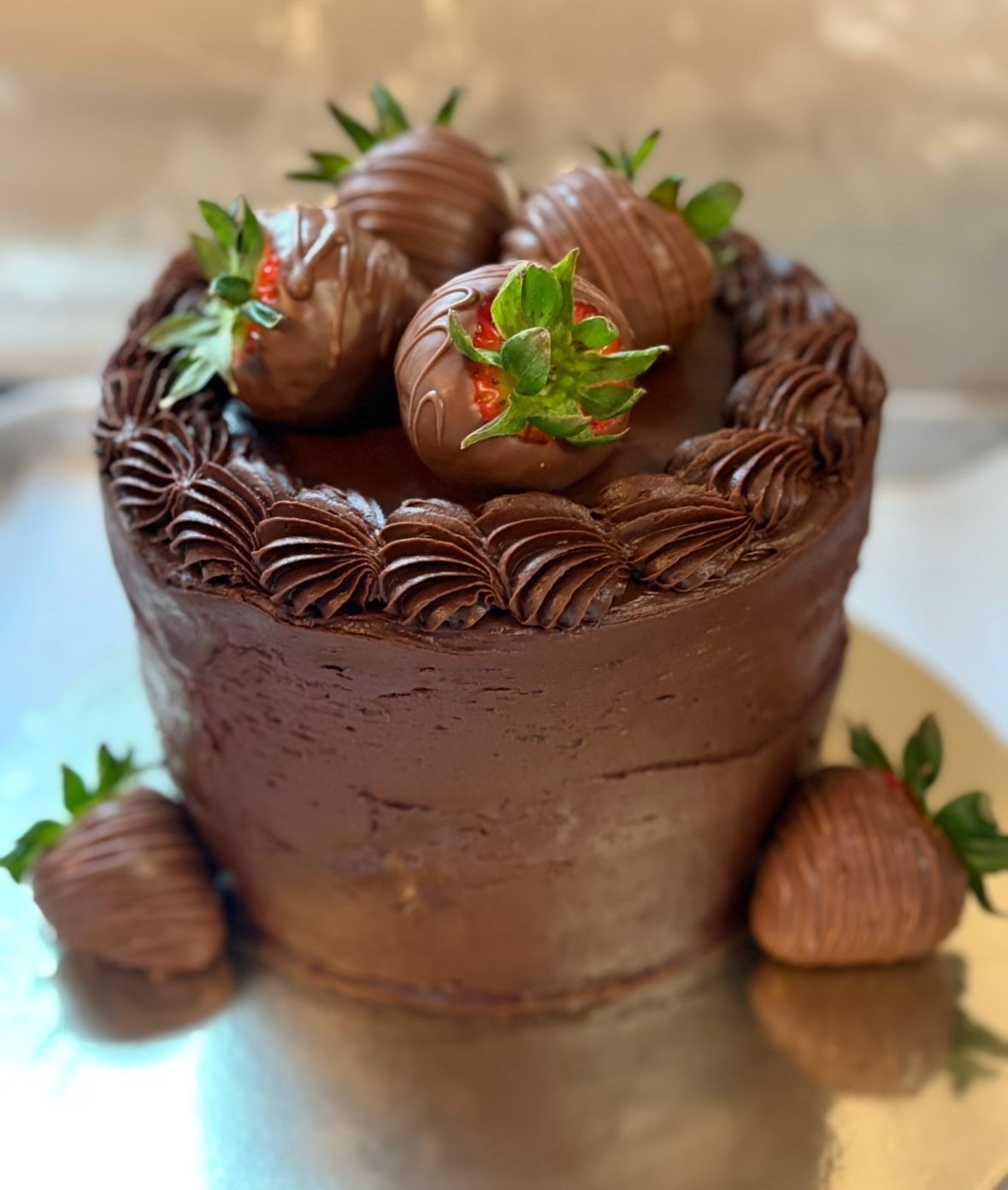 Chocolate cake with chocolate-covered strawberries on top and around the base, on a silver cake stand.