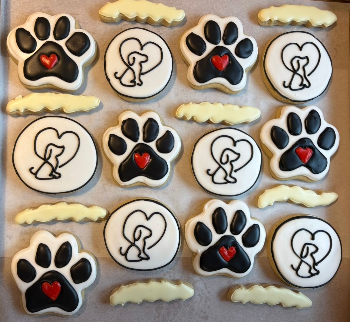 Tray of decorated dog-themed cookies: paw prints with hearts, dogs in hearts, and cloud shapes.