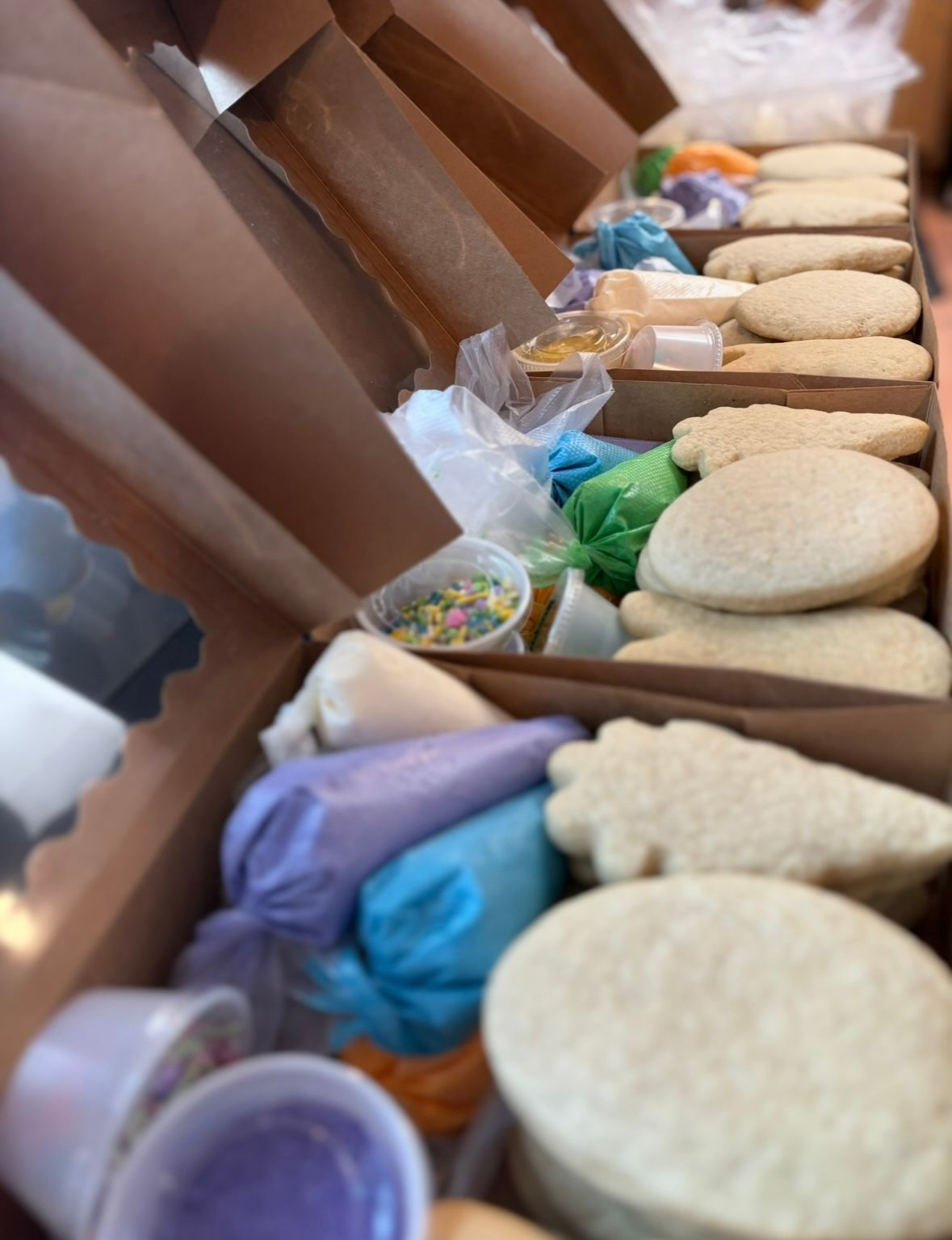 Cookie decorating kits in open cardboard boxes, with cookies, icing bags, and sprinkles.