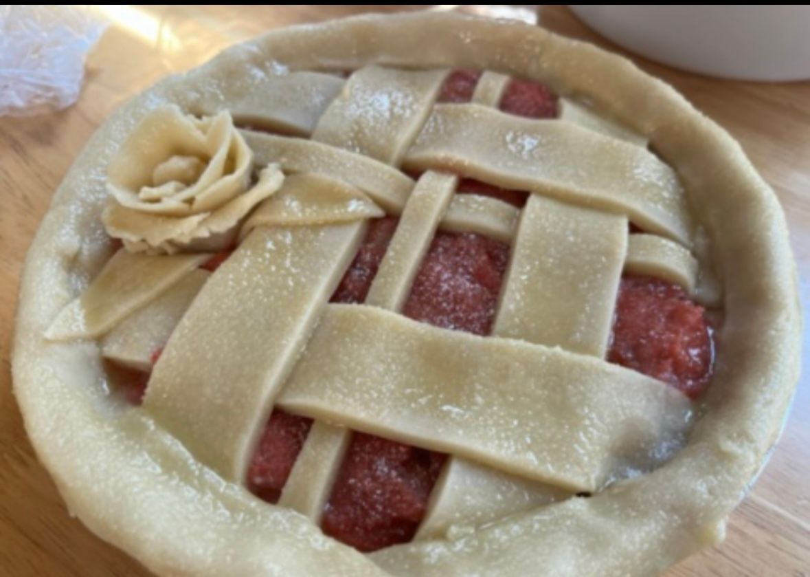 Mini pie with lattice crust and dough rose, filled with red filling, on wooden surface.