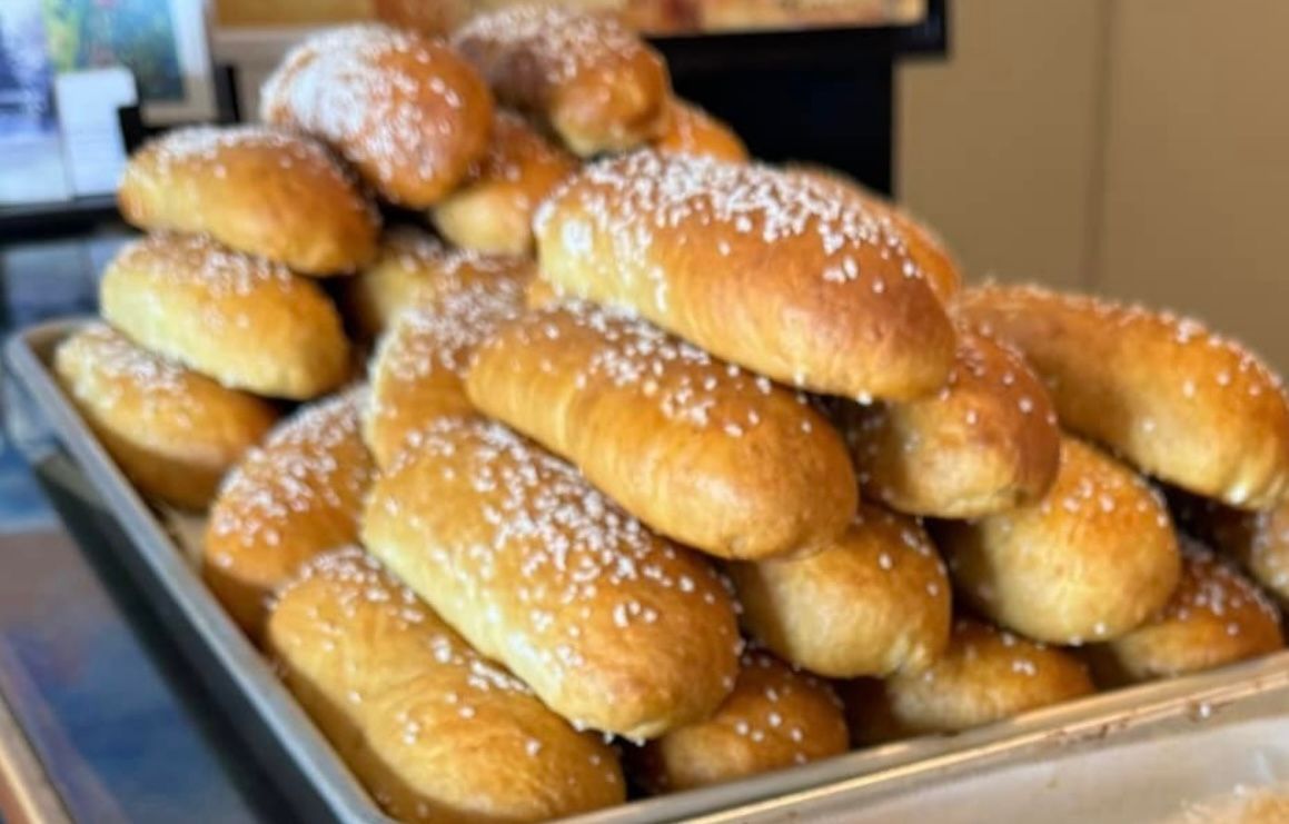 Pile of golden-brown pretzel rolls sprinkled with coarse salt on a baking sheet.