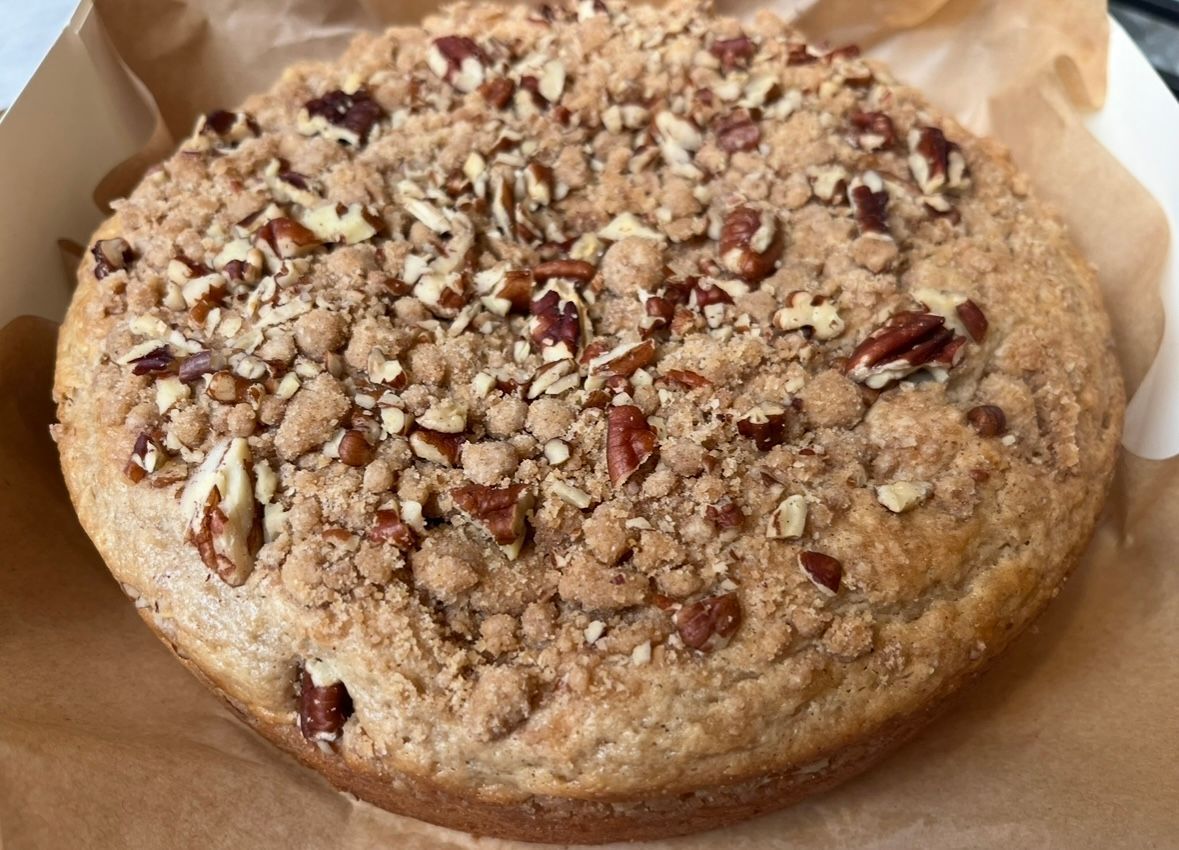 Coffee cake with pecan topping in a paper-lined container.