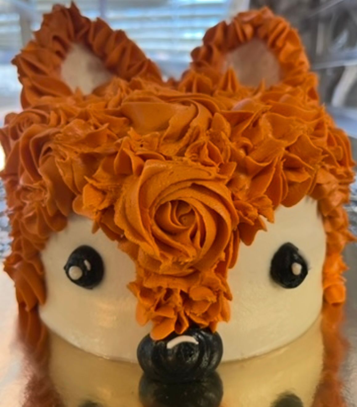 Fox-shaped cake decorated with orange frosting fur, white face, black eyes, and nose.