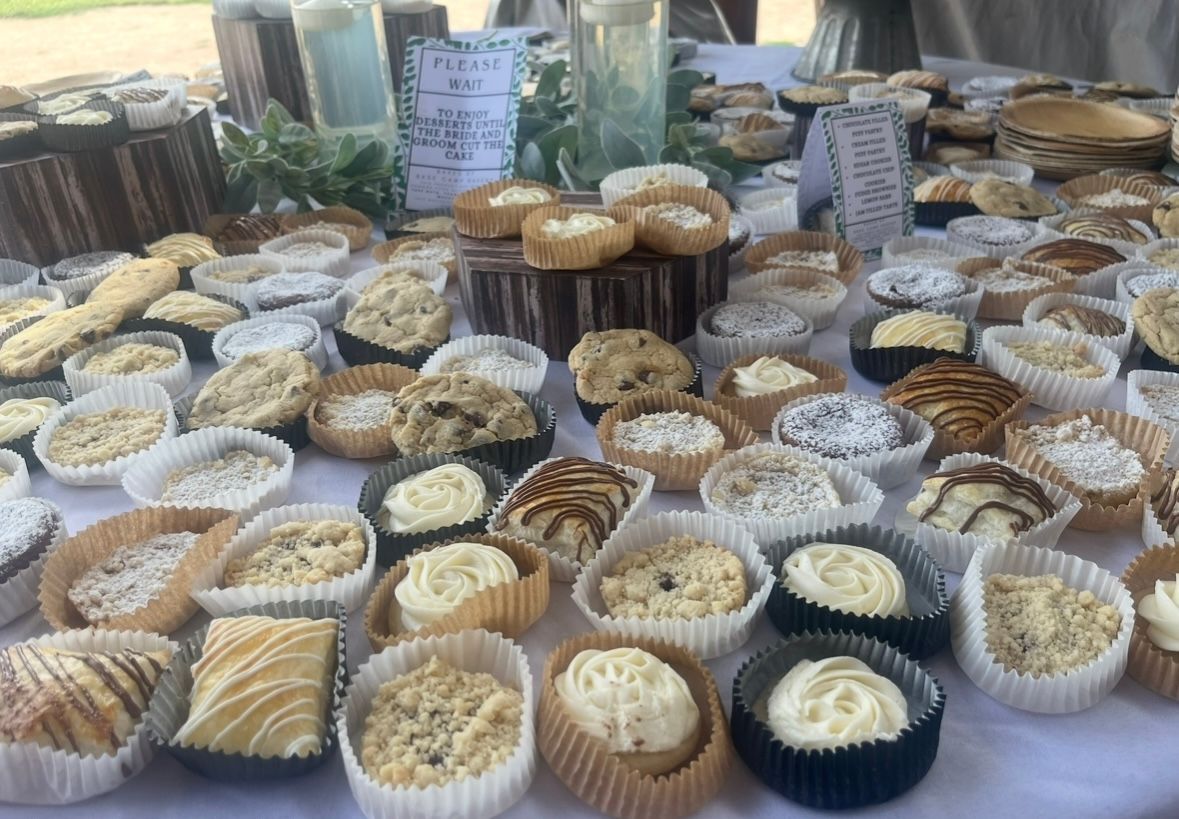 Baked goods display on a table, including cupcakes, muffins, and cookies in paper liners.