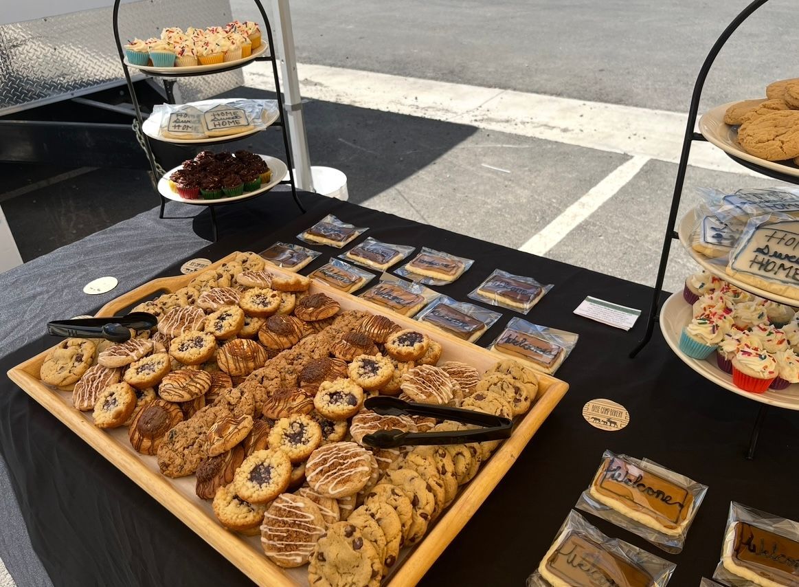 Dessert display: cookies, brownies, and cupcakes on tiered stands, black tablecloth, outdoor setting.