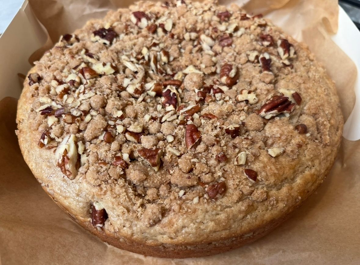 Round coffee cake with pecan topping in a bakery box.