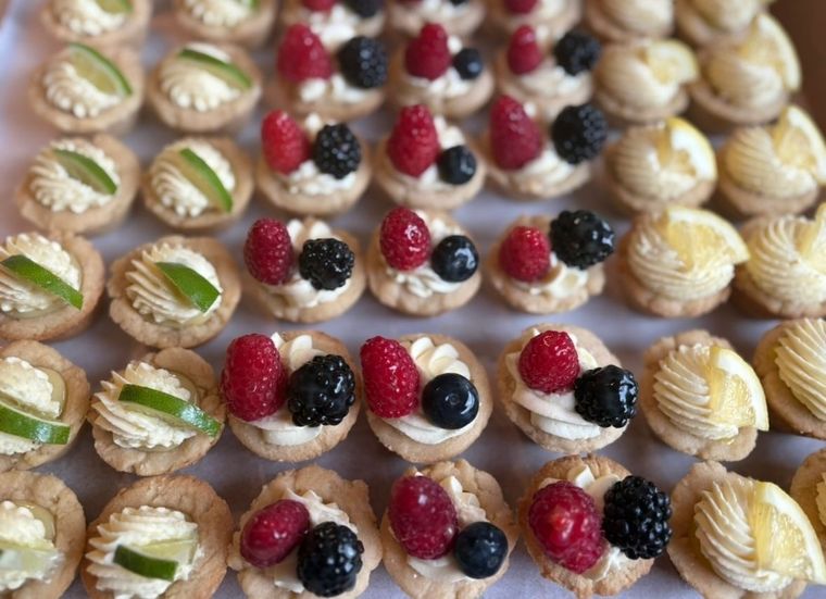 Mini pastries topped with fruit, cream, and lime in a tray.