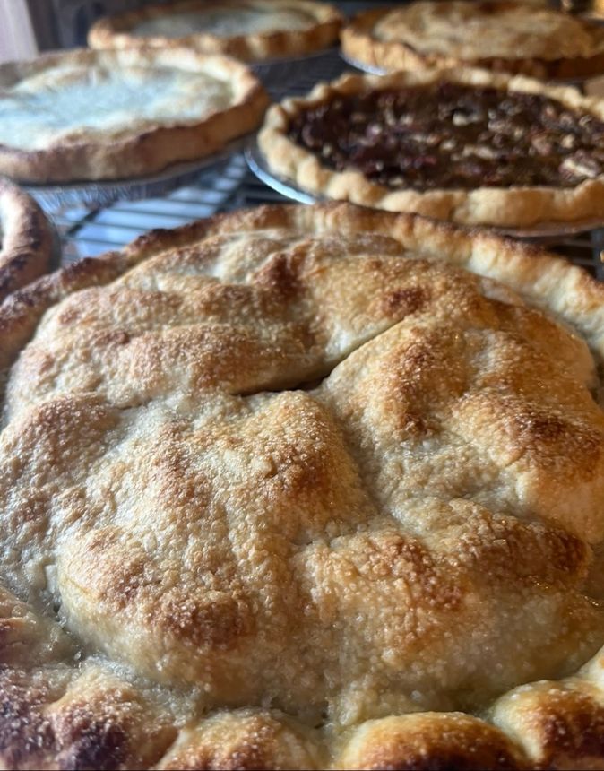Close-up of a golden-brown pie crust with several other pies on a wire rack in the background.