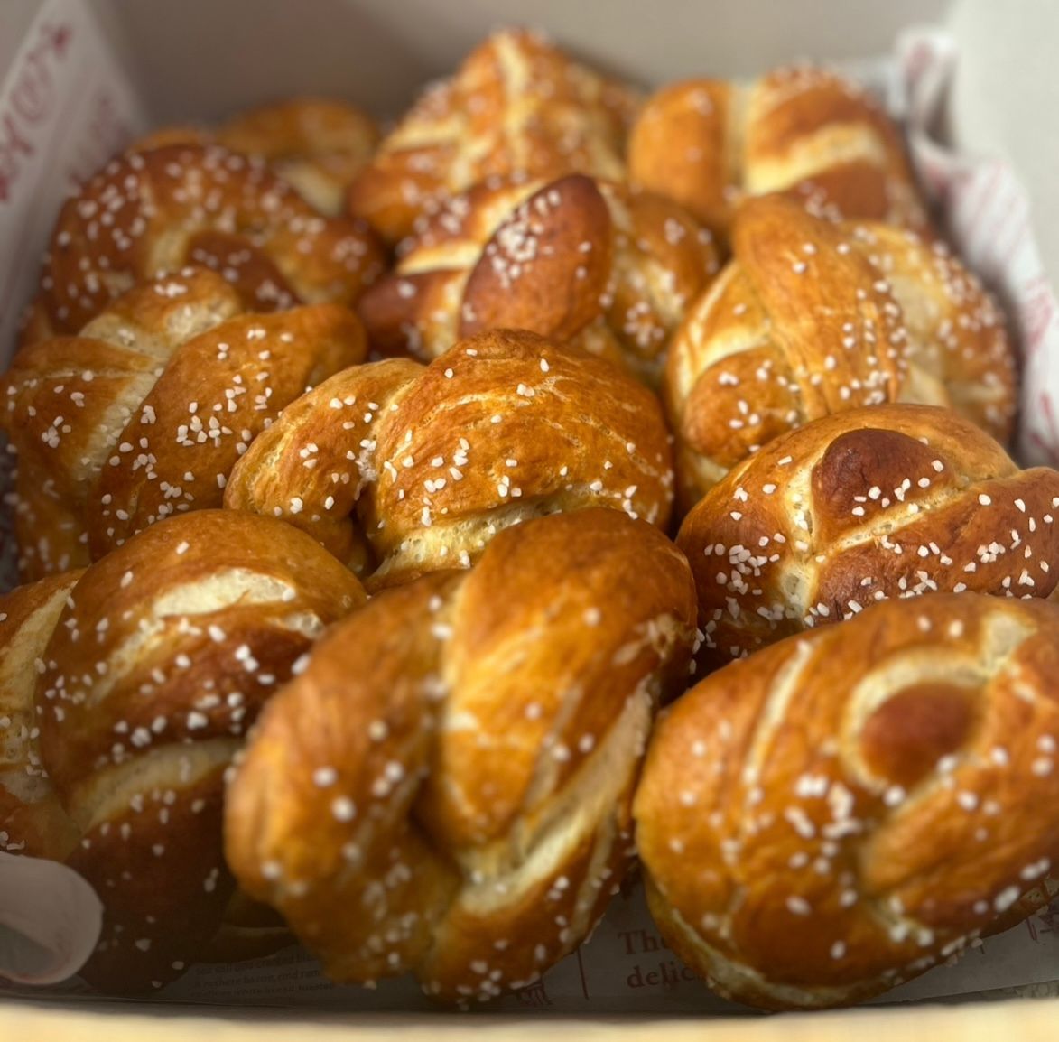 Box of golden-brown pretzels, sprinkled with coarse salt, ready to eat.