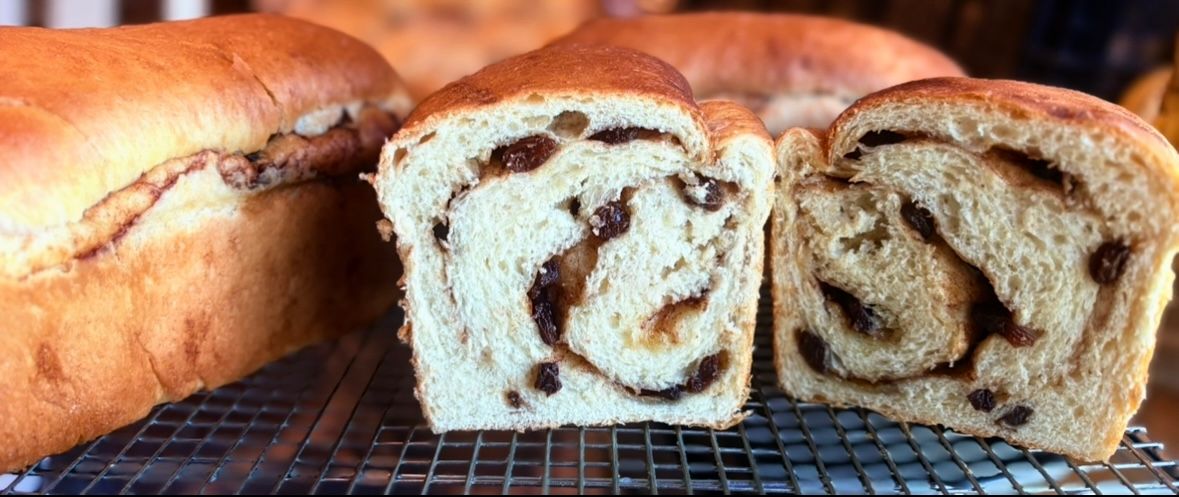 Loaves of cinnamon raisin bread, one sliced open, on a wire rack.