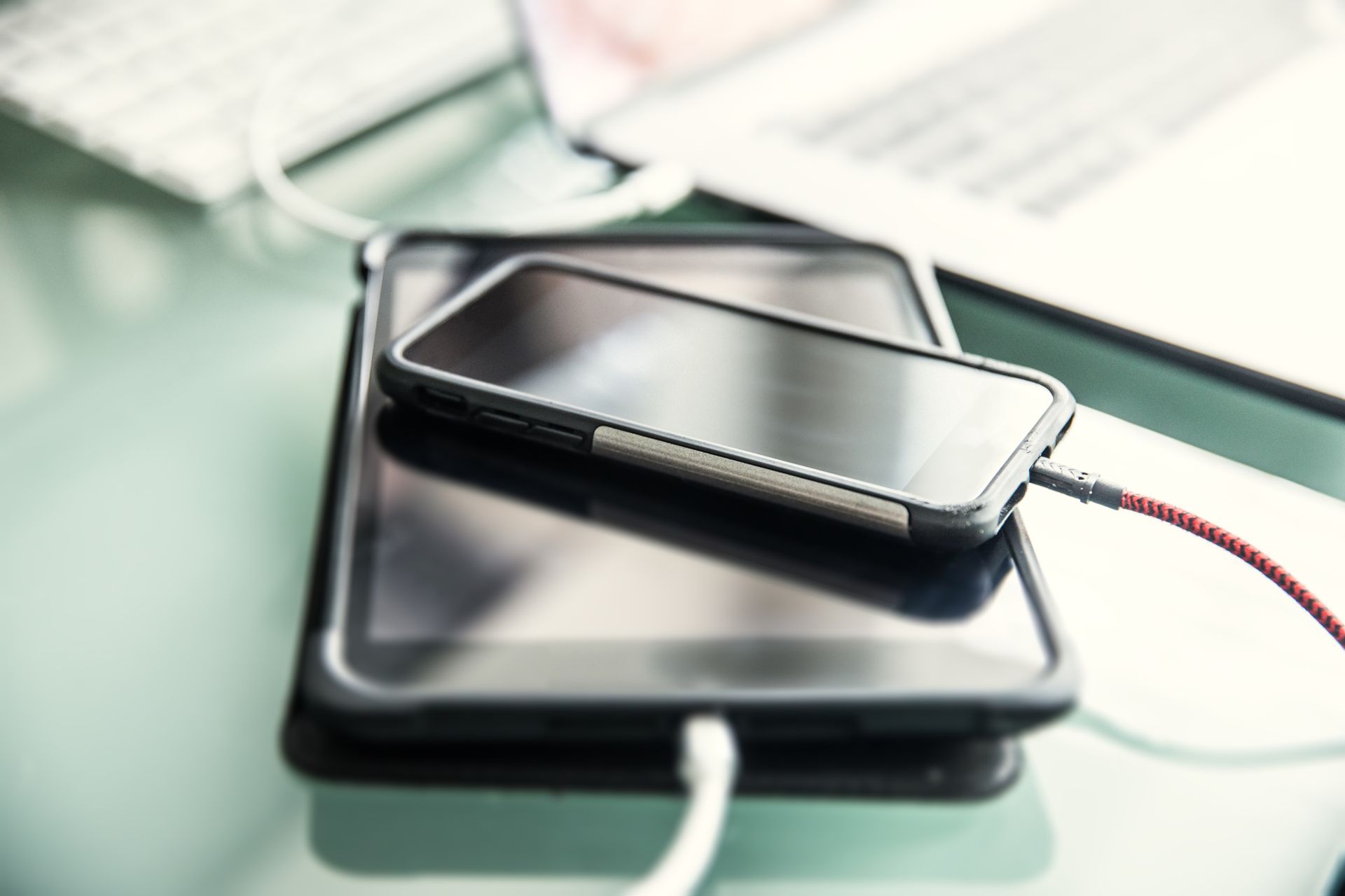 Smartphone charging on top of a tablet; both connected with charging cables.