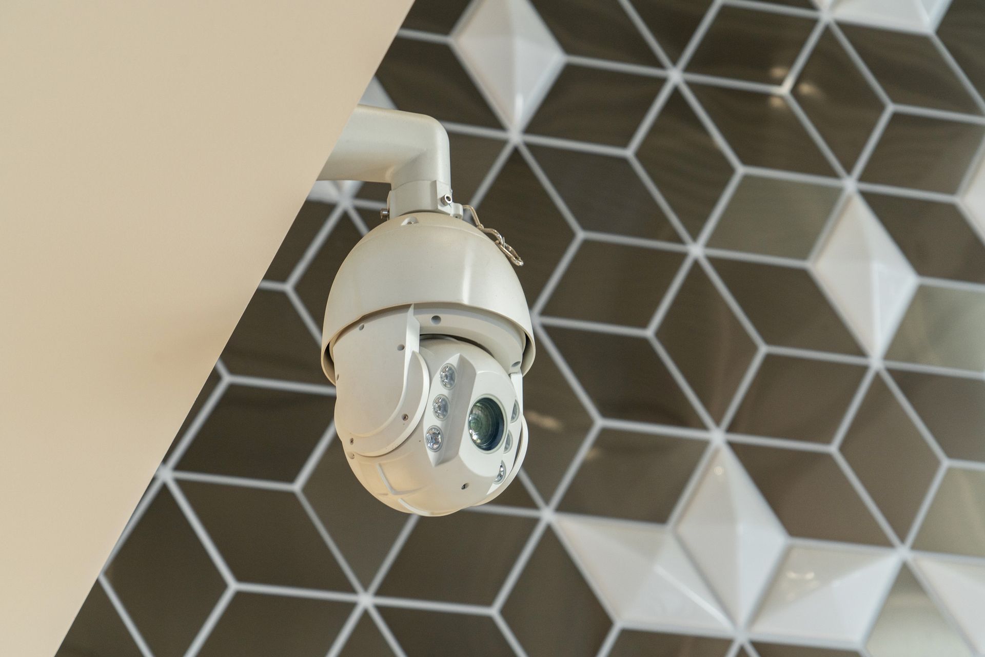 White security camera mounted on a wall with geometric tiles.