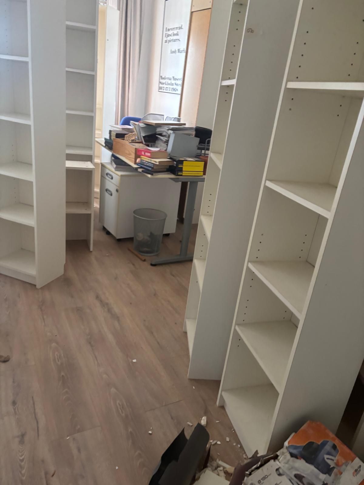 Tre librerie bianche in una stanza con scrivania e pavimento in legno.