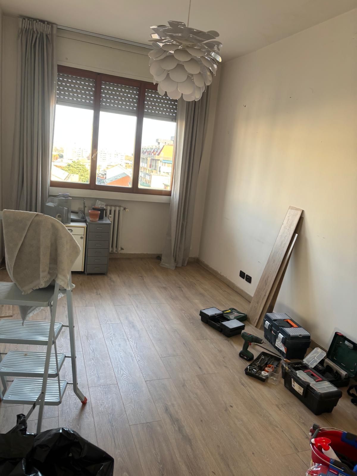 Stanza vuota con attrezzi, assi di legno, finestra e lampadario sospeso.