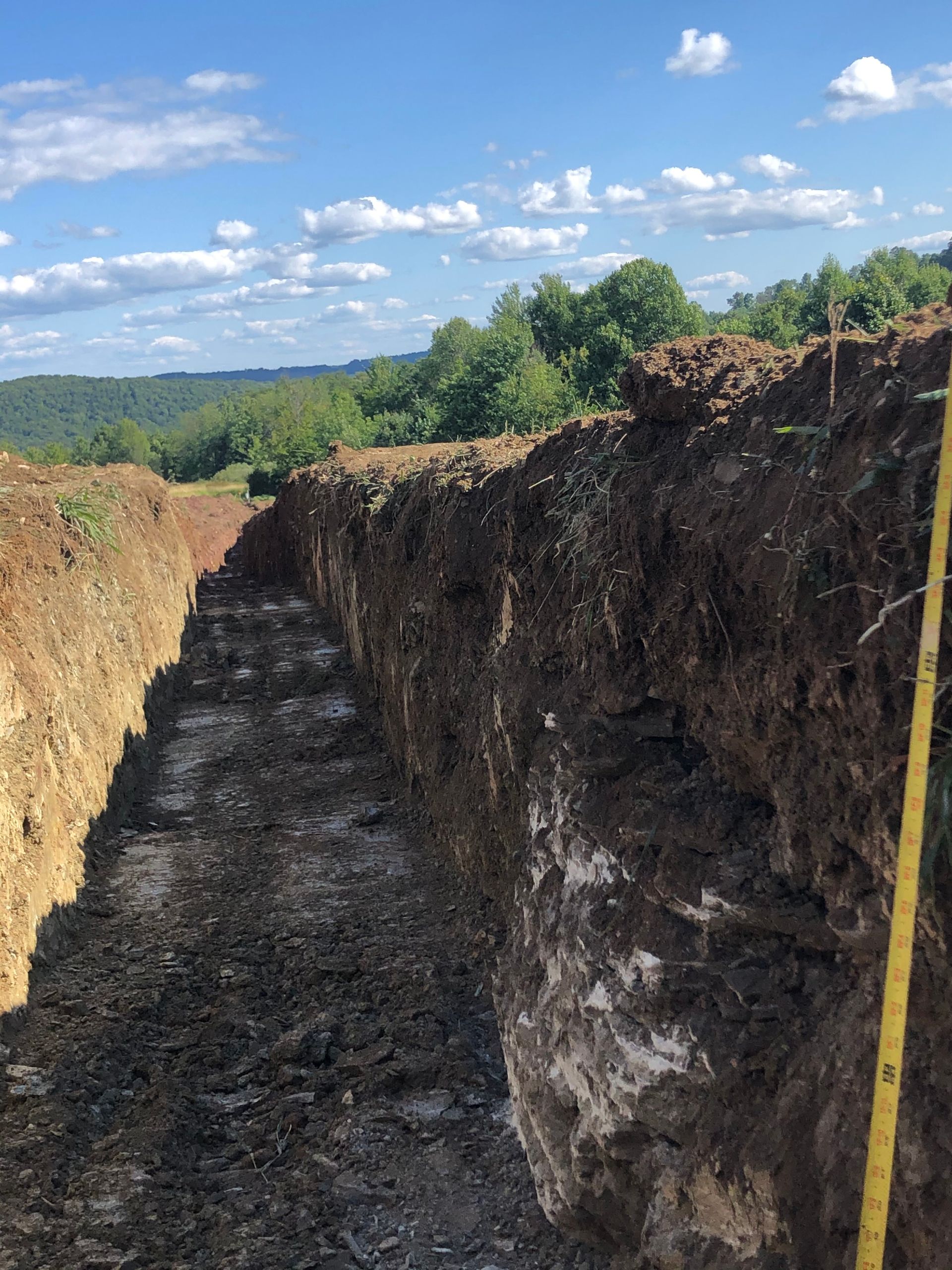 A Person is Measuring a Trench With a Tape Measure