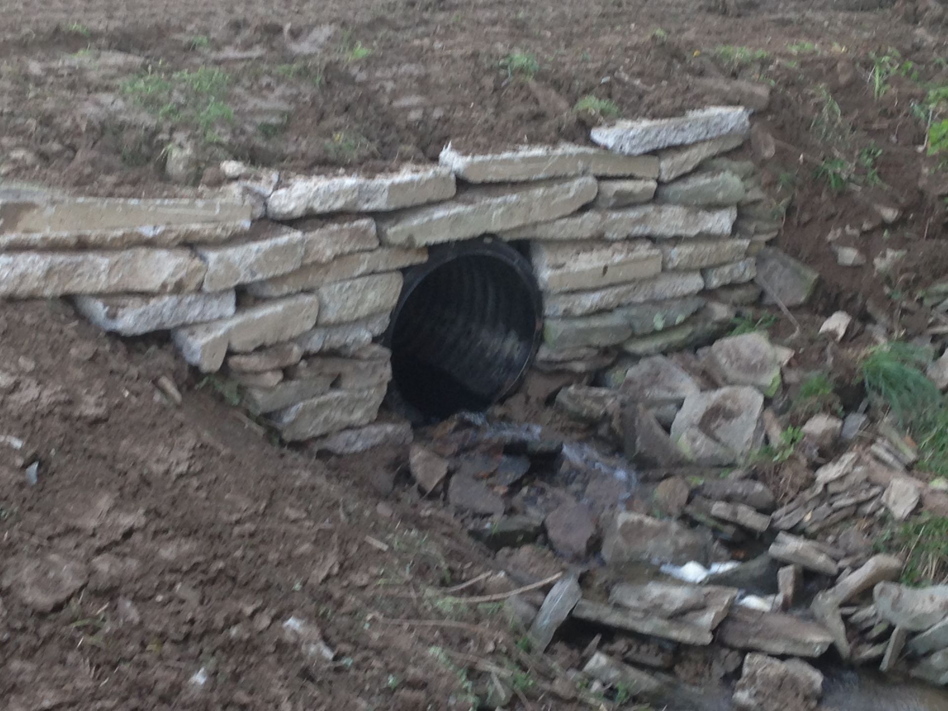 A Pipe is Going Through a Stone Wall Next to a Stream