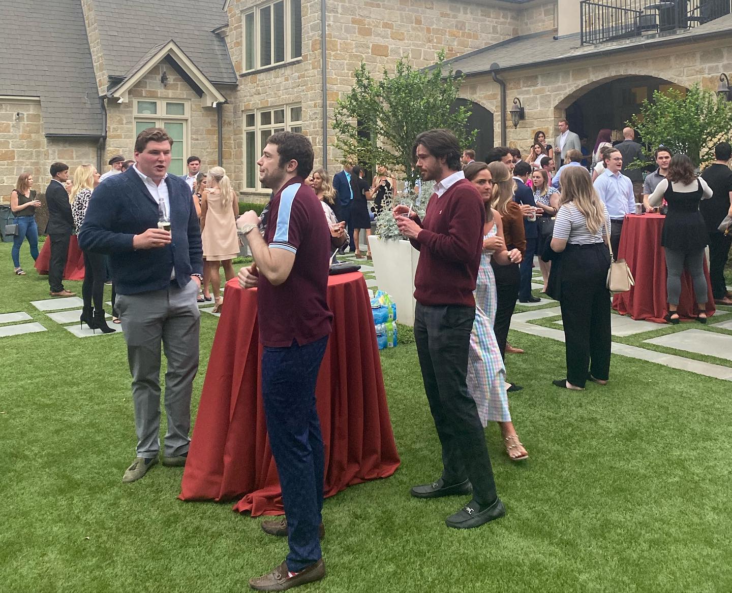 A group of people are standing around tables on a lush green field.