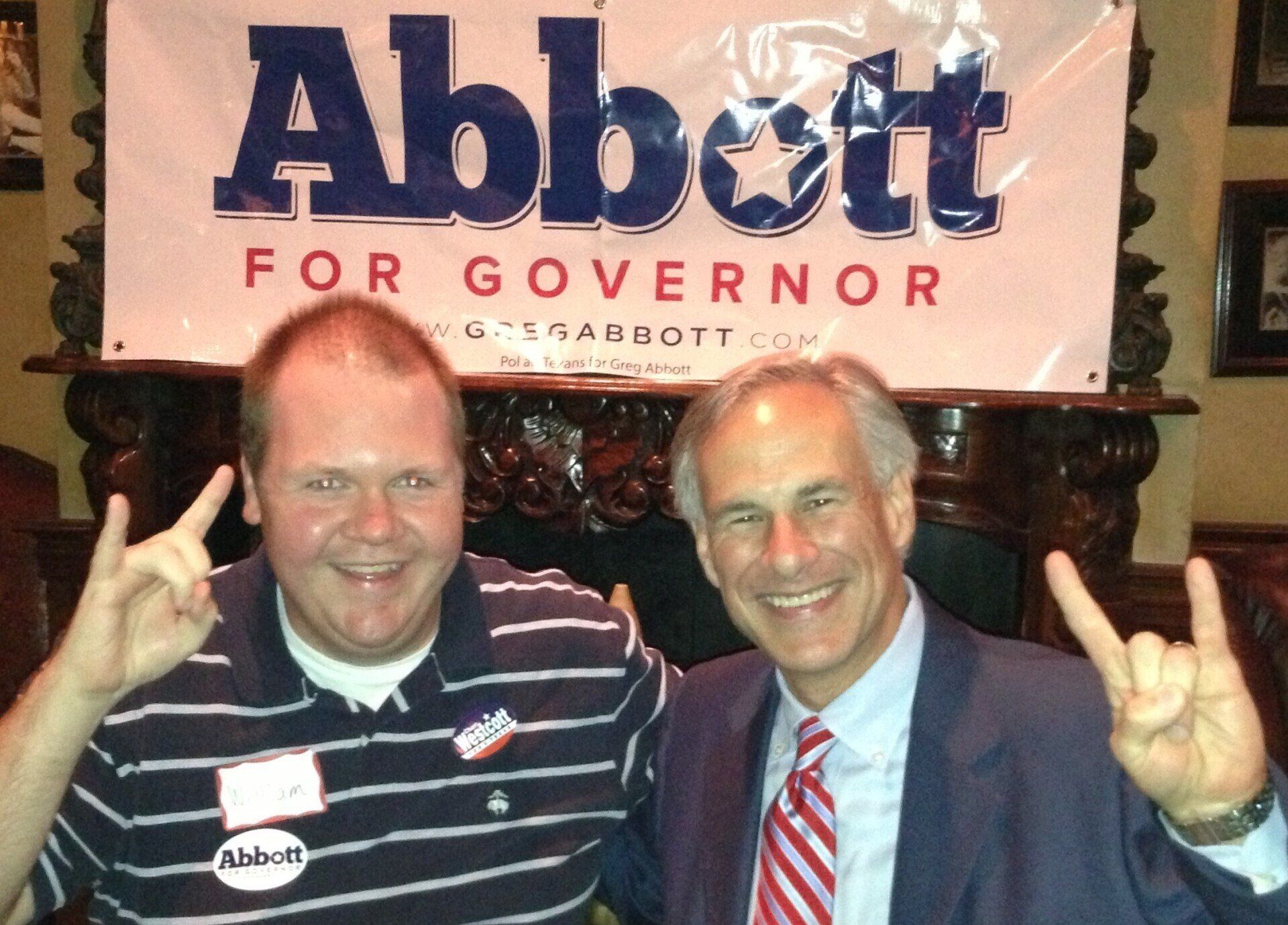 Two men pose in front of a sign that says abbott for governor