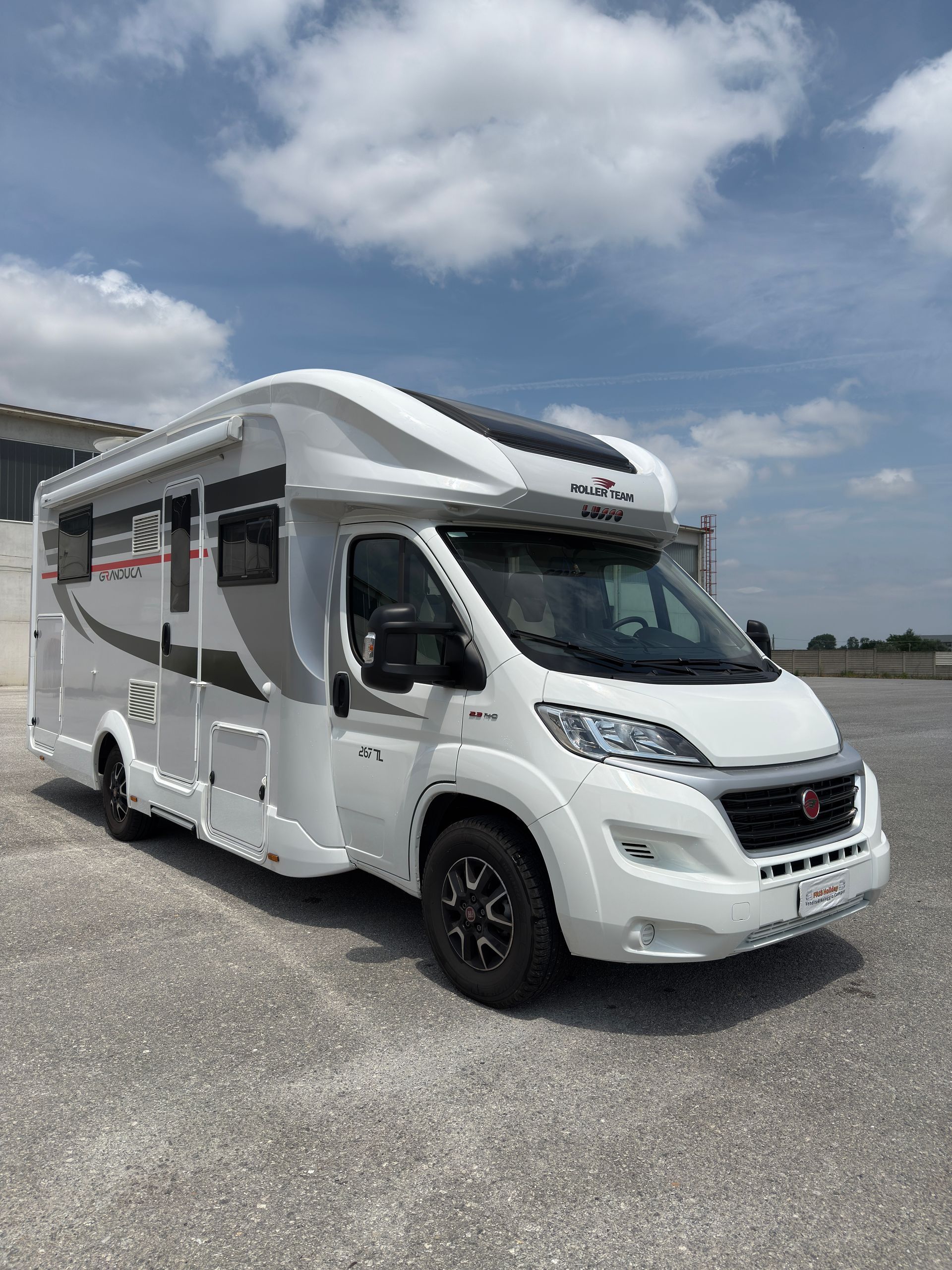 Camper bianco parcheggiato sulla ghiaia sotto un cielo nuvoloso.