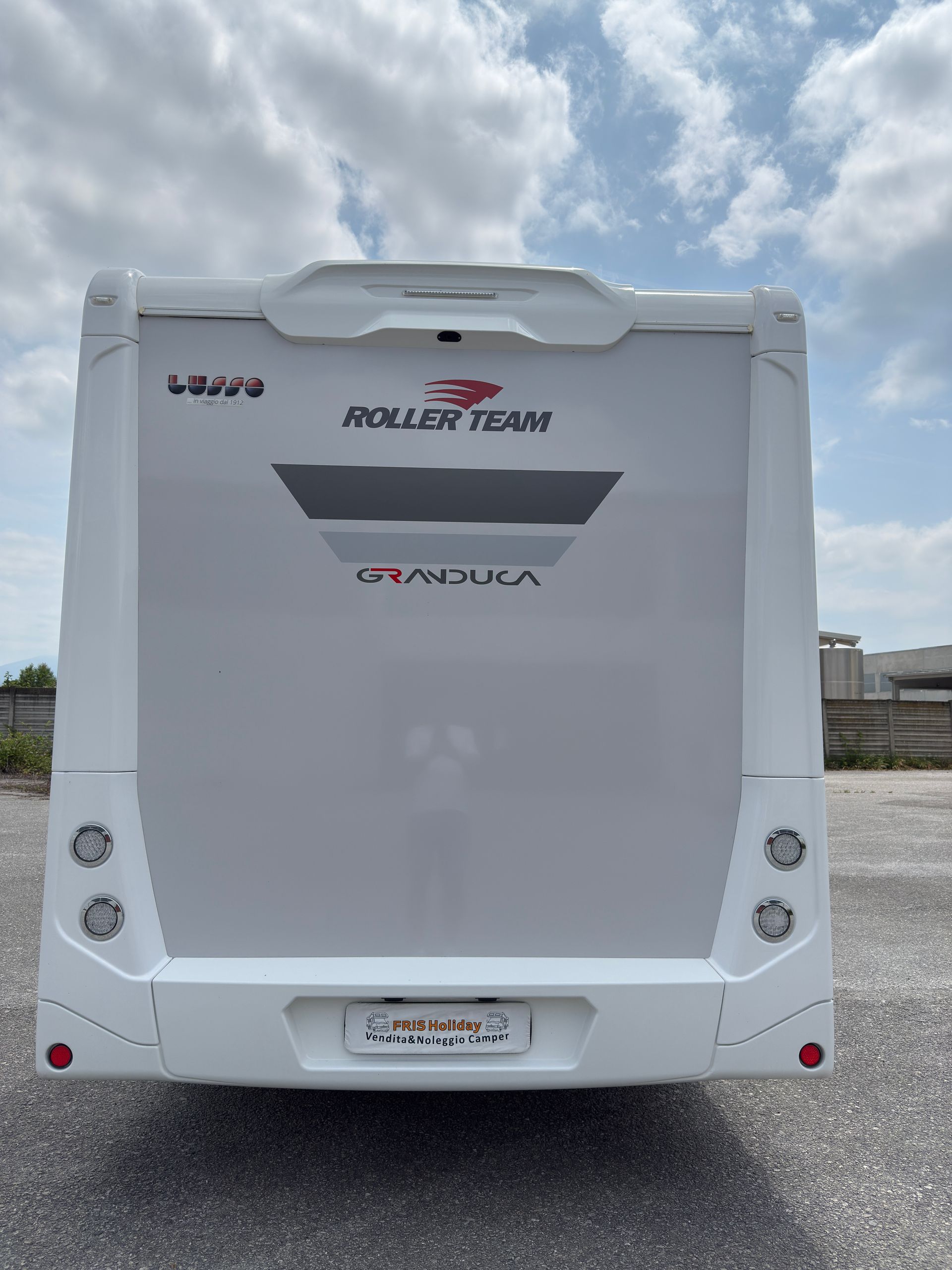 Vista posteriore di un camper bianco del Roller Team con logo, targa e luci posteriori sotto un cielo nuvoloso.