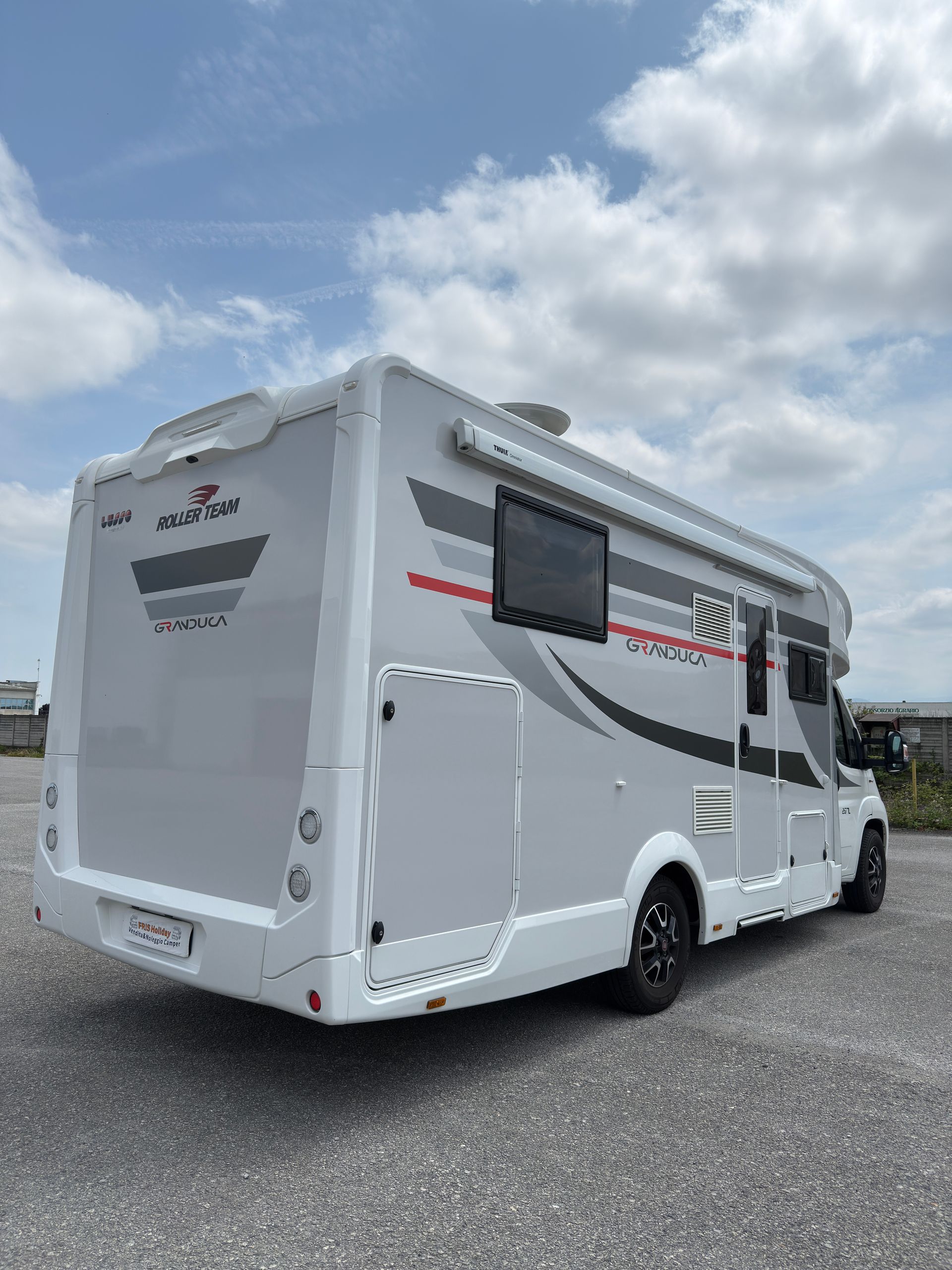 Veicolo ricreativo grigio e bianco con dettagli neri parcheggiato all'aperto sotto un cielo azzurro.