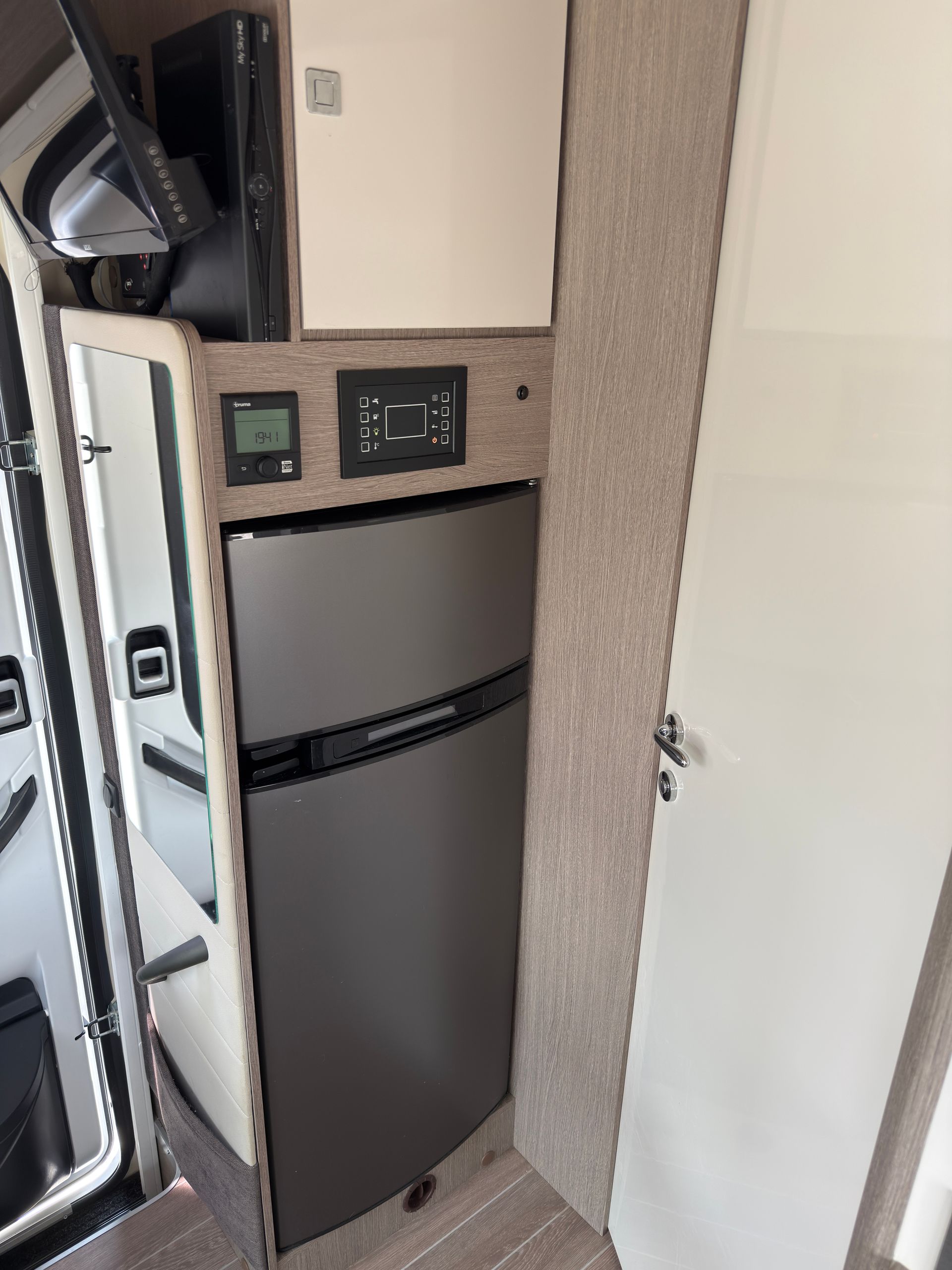 Vista interna di un furgone con frigorifero, mobiletto e pannelli di controllo.