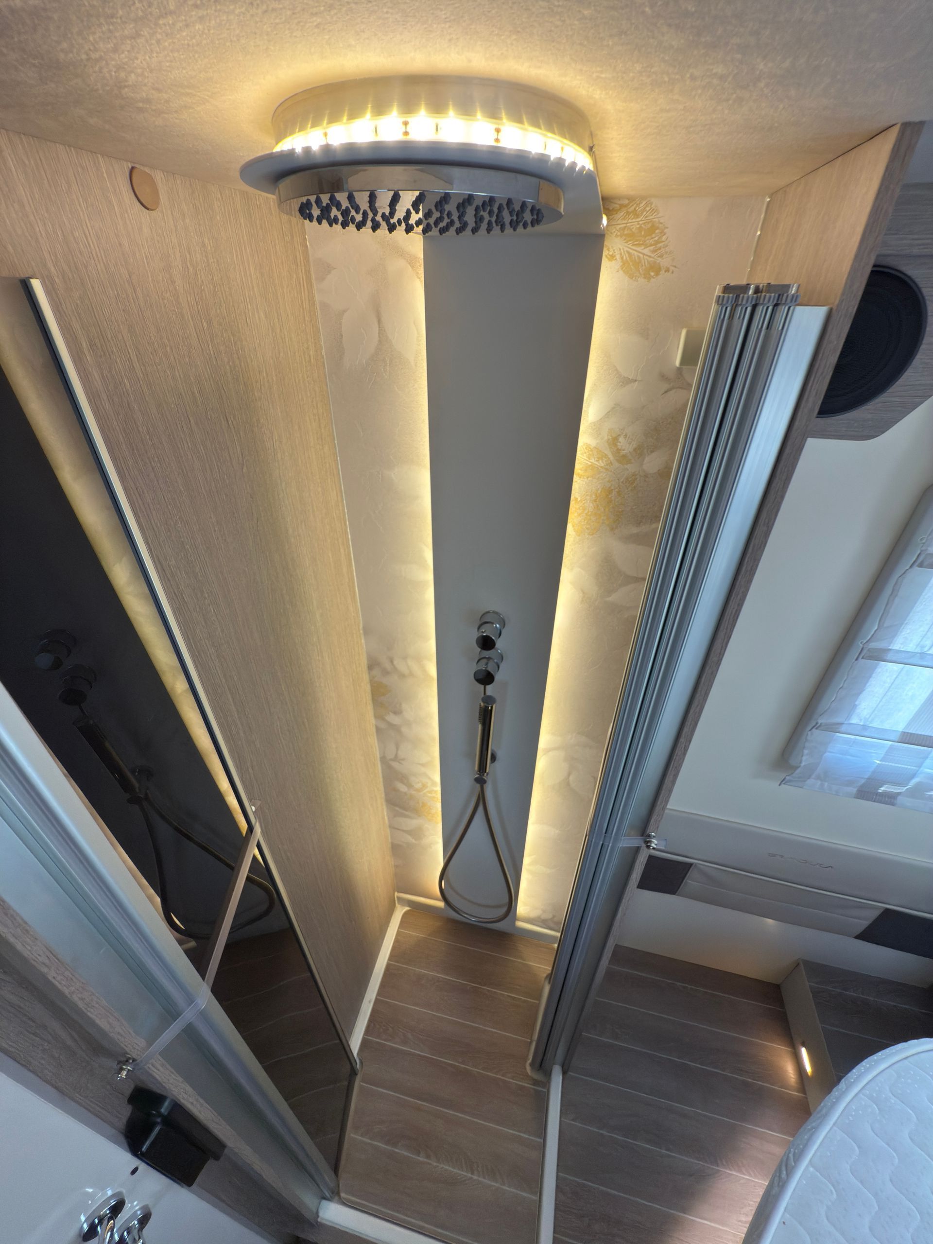 Doccia con soffione, illuminazione da incasso e pavimento in legno in un bagno moderno.