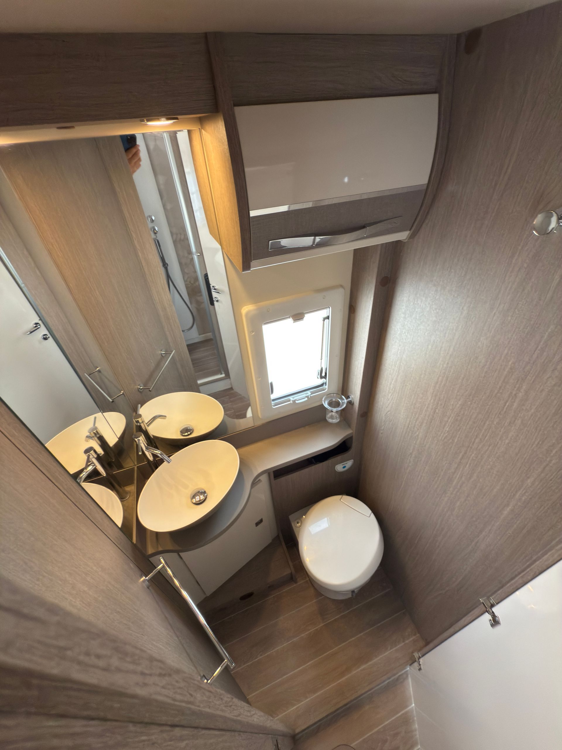 Piccolo bagno per camper con WC, lavandino, specchio e finestra.