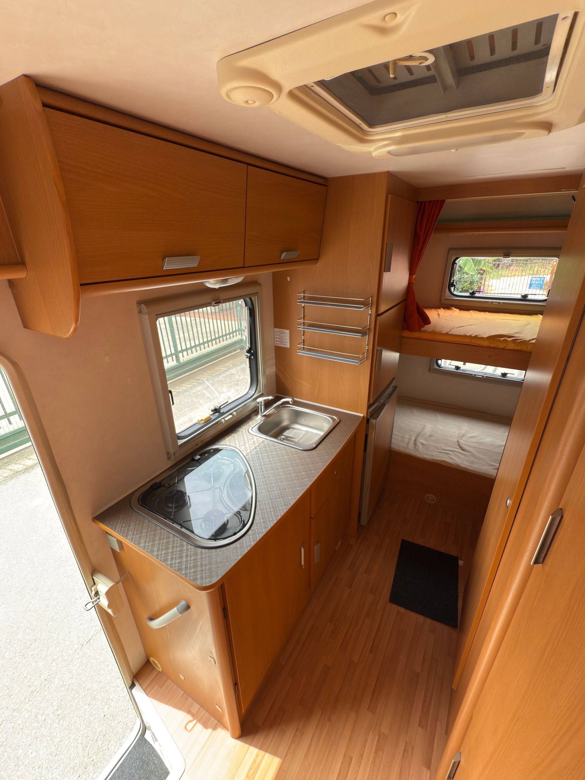Interno di un camper con cucina, armadietti, lavello, fornello e vista sulla zona giorno.