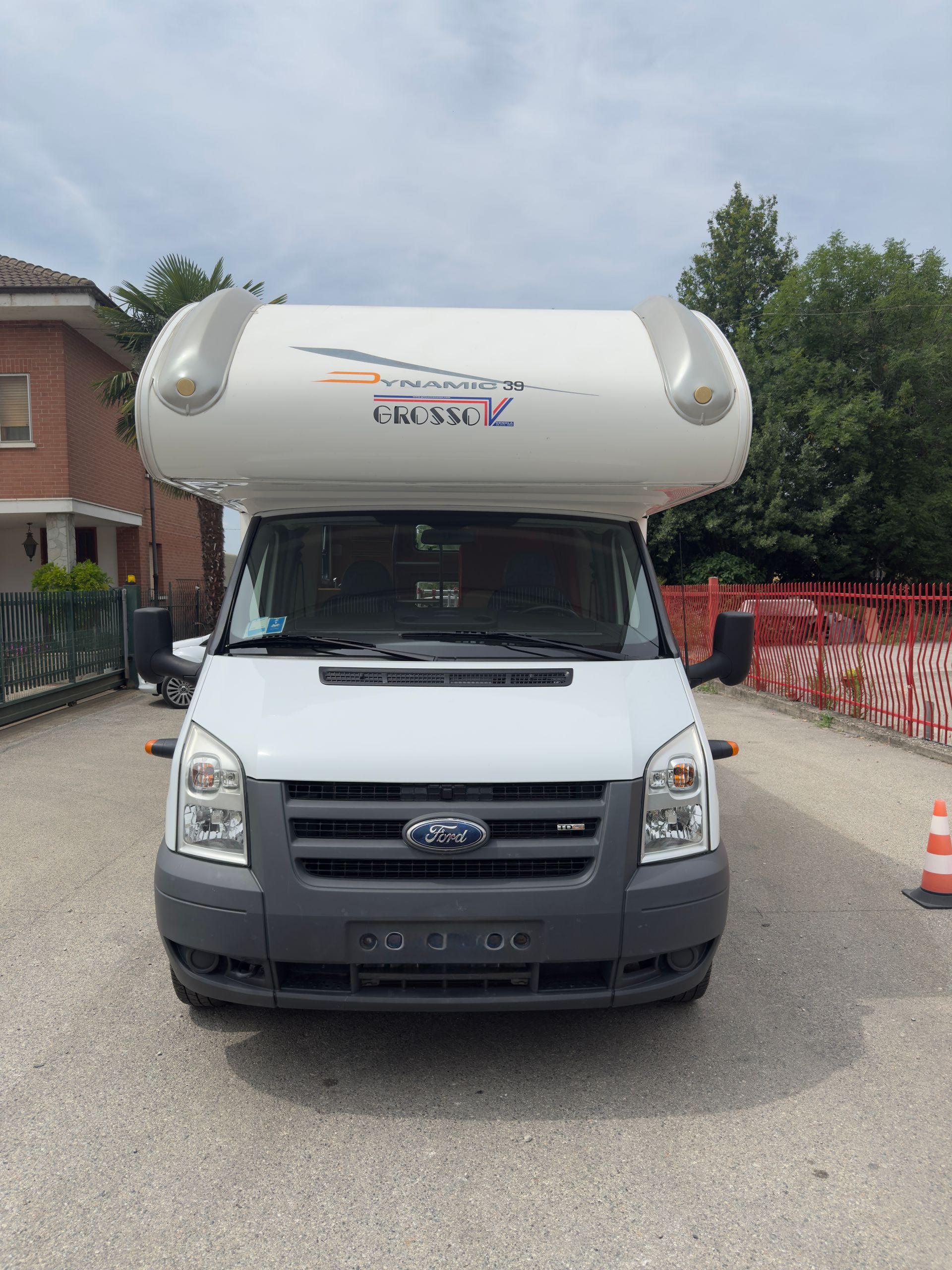 Camper bianco parcheggiato su una strada sterrata con case sullo sfondo.