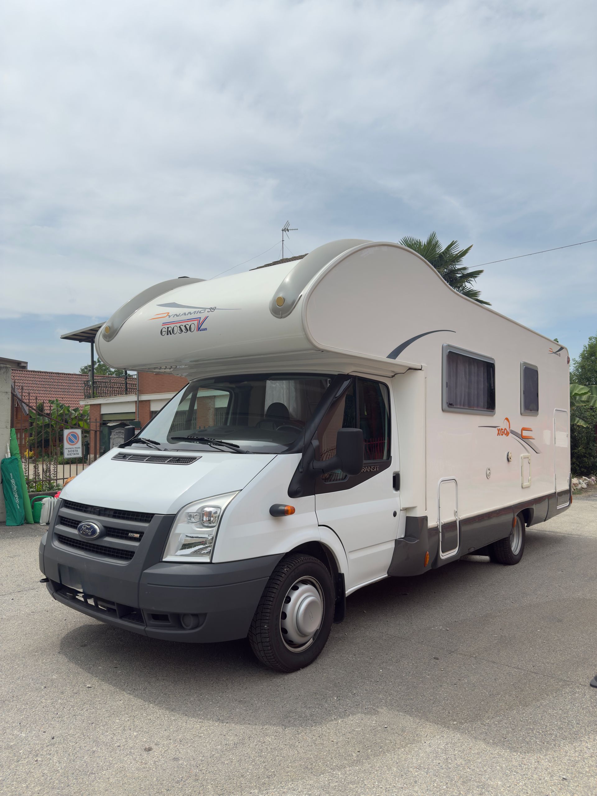 Camper bianco parcheggiato sulla ghiaia sotto un cielo nuvoloso.