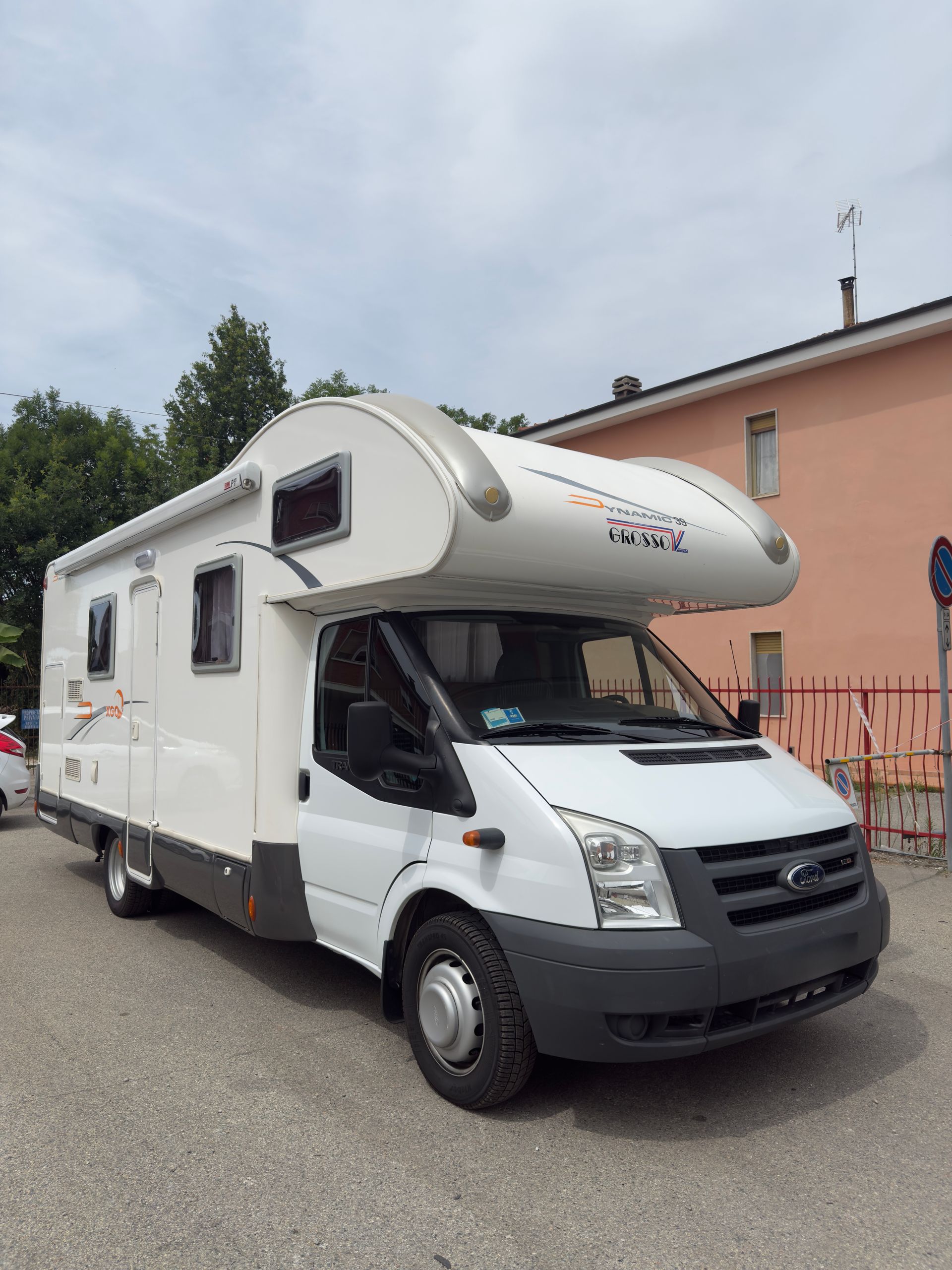 Veicolo ricreativo bianco parcheggiato davanti a un edificio in una giornata di sole.