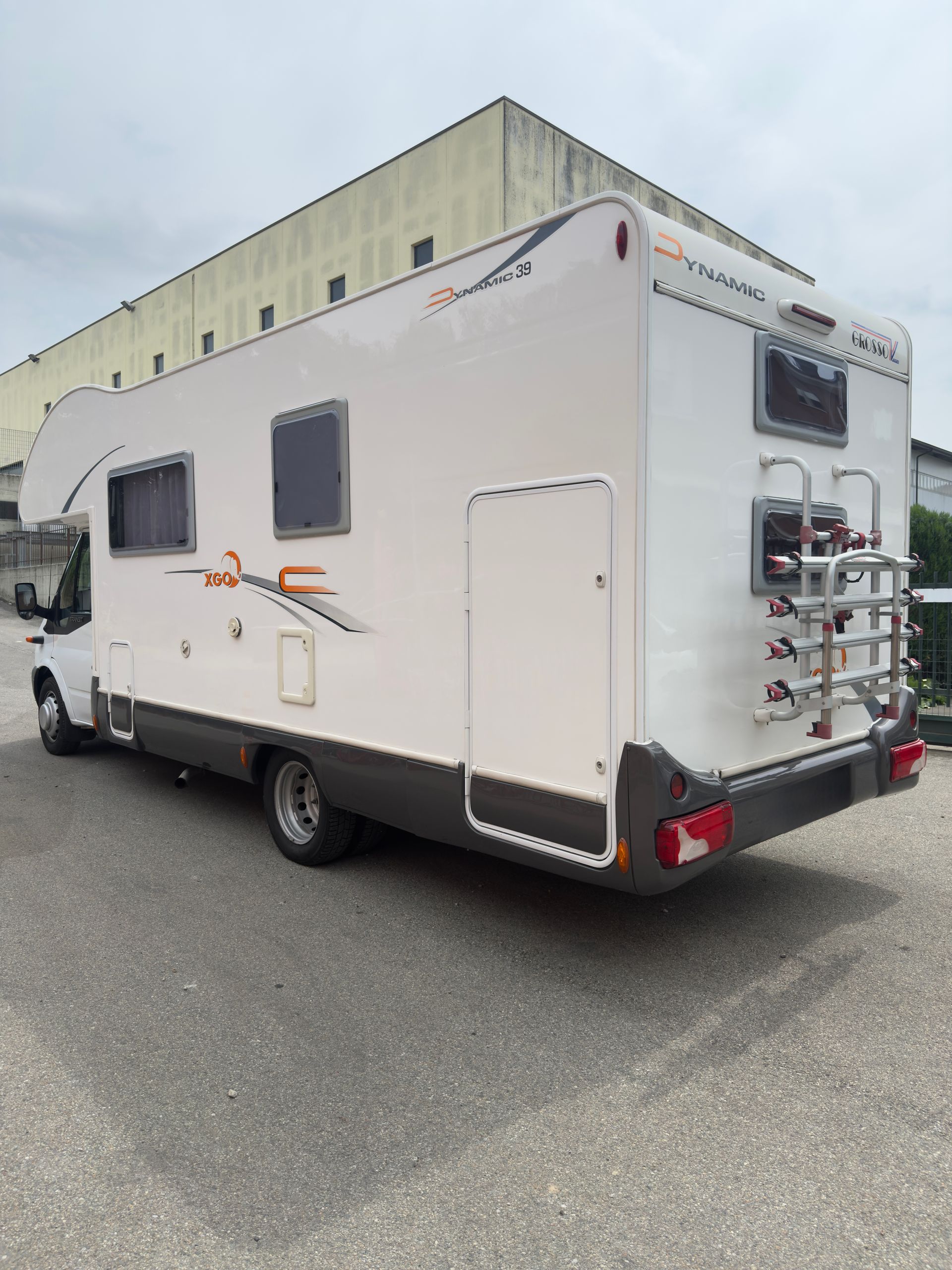 Camper bianco parcheggiato all'aperto, con portabiciclette sul retro.
