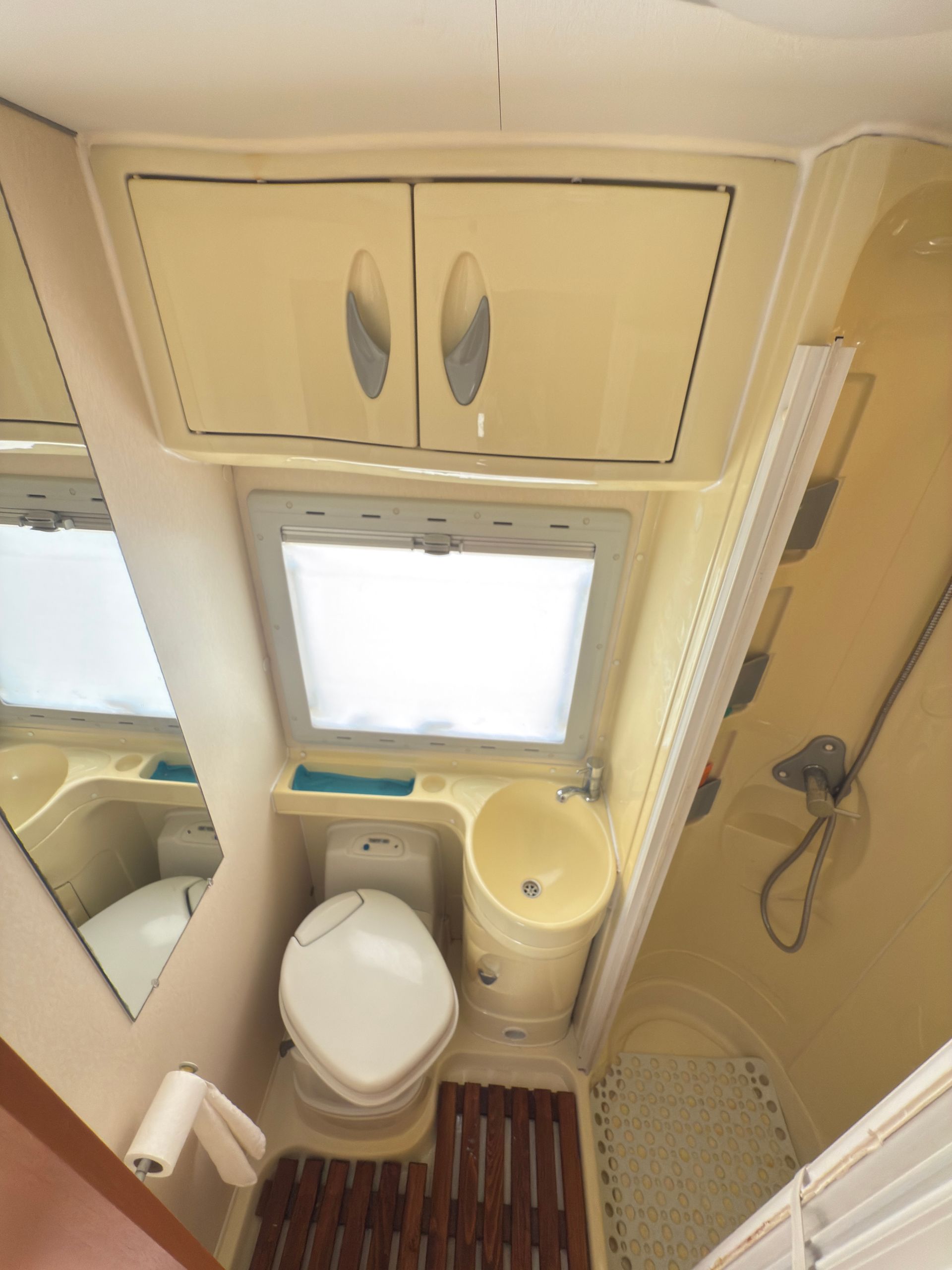 Piccolo bagno per camper con WC, lavandino, doccia e armadietti.