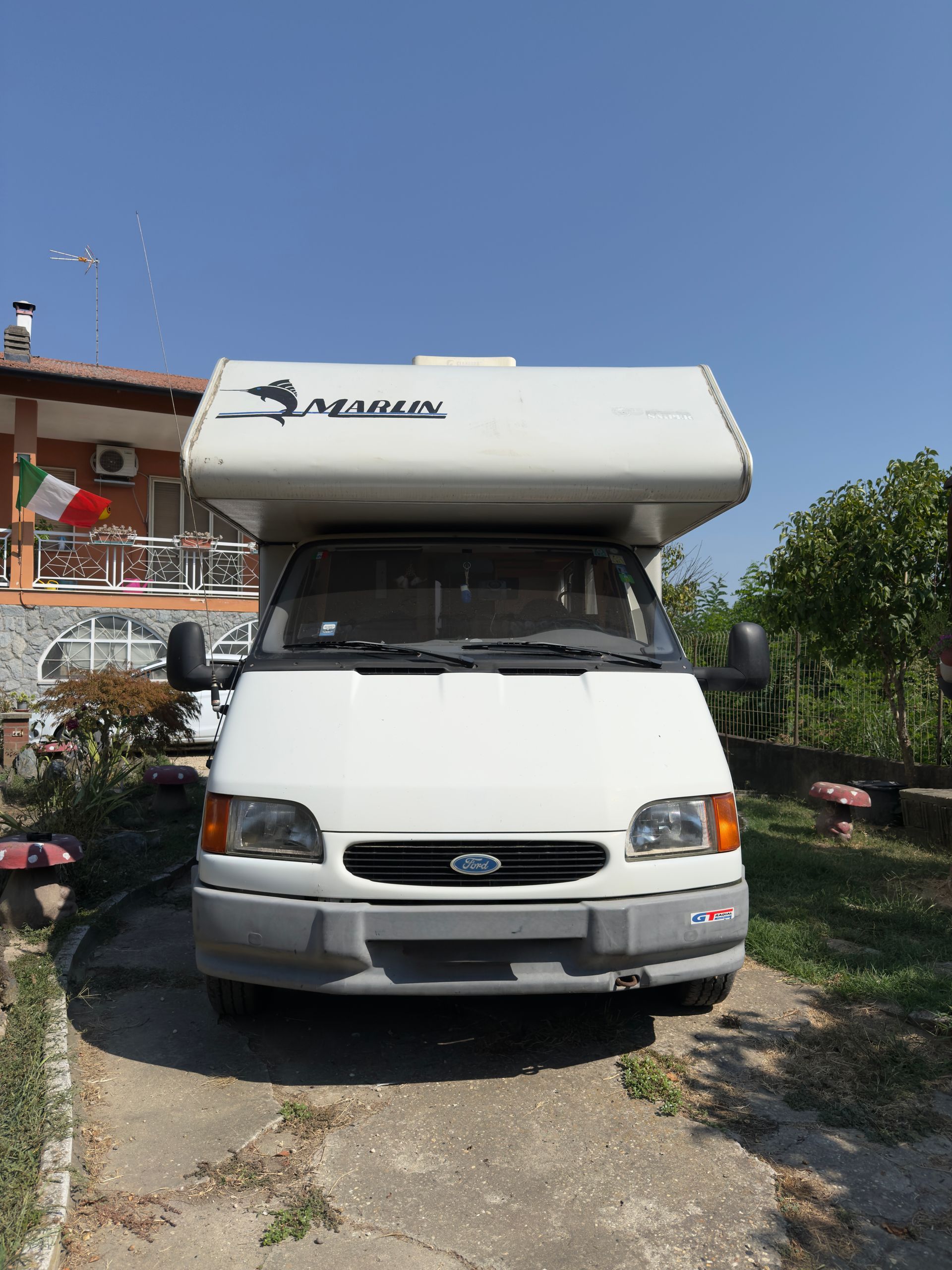 Camper bianco parcheggiato davanti a un edificio con una bandiera italiana.