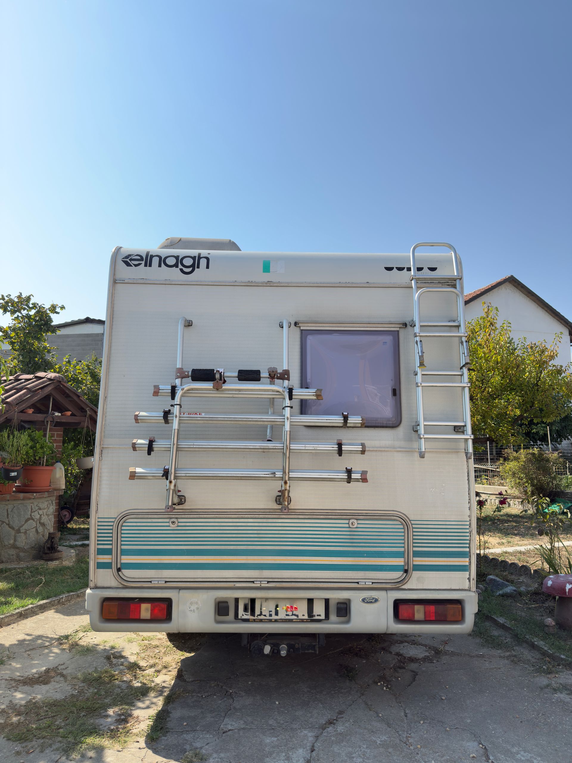 Vista posteriore di un camper bianco Elnagh con portabici e scala, parcheggiato all'aperto sotto un cielo azzurro.