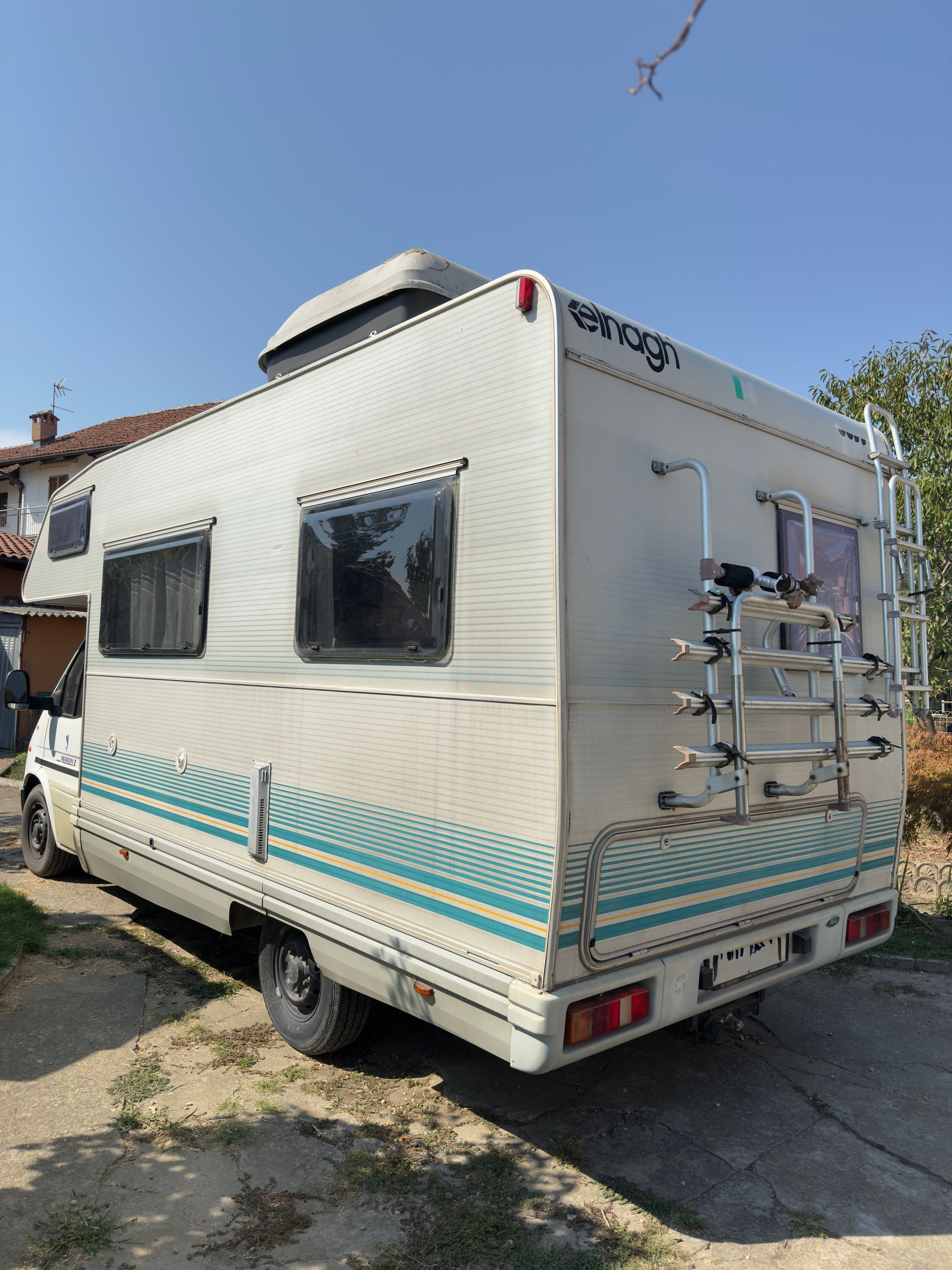 Camper bianco con strisce color verde acqua parcheggiato all'aperto in una giornata di sole.